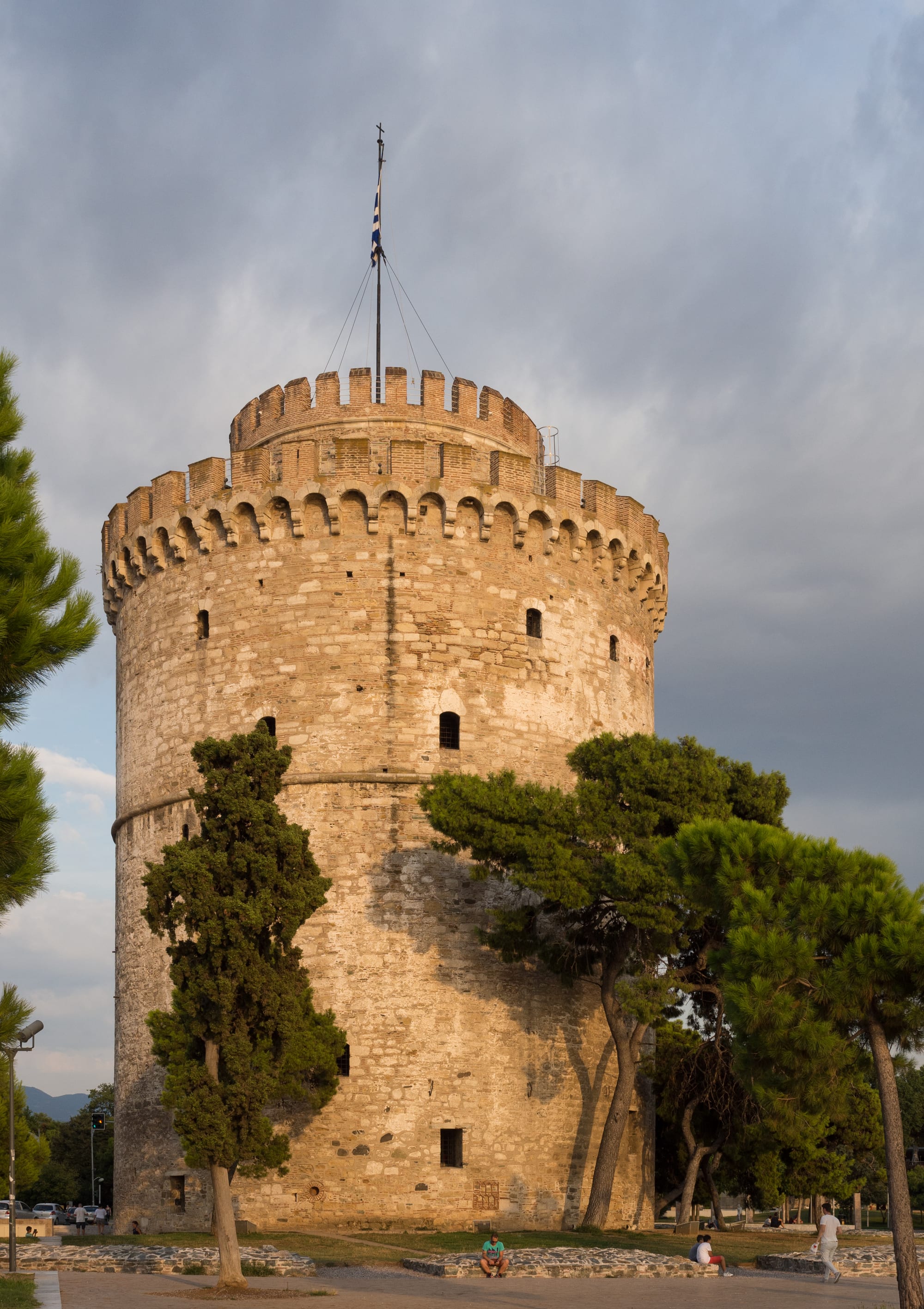 A cylindrical stone tower on a city waterfront promenade