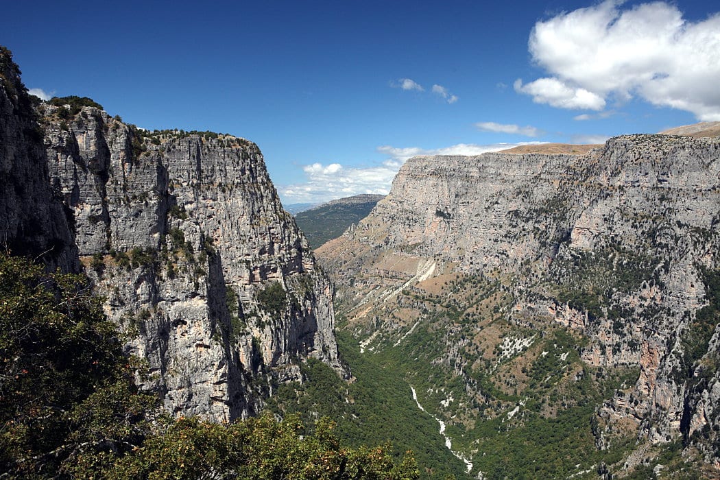 A vast steep-sided gorge of grey rock and green forest seen from a clifftop