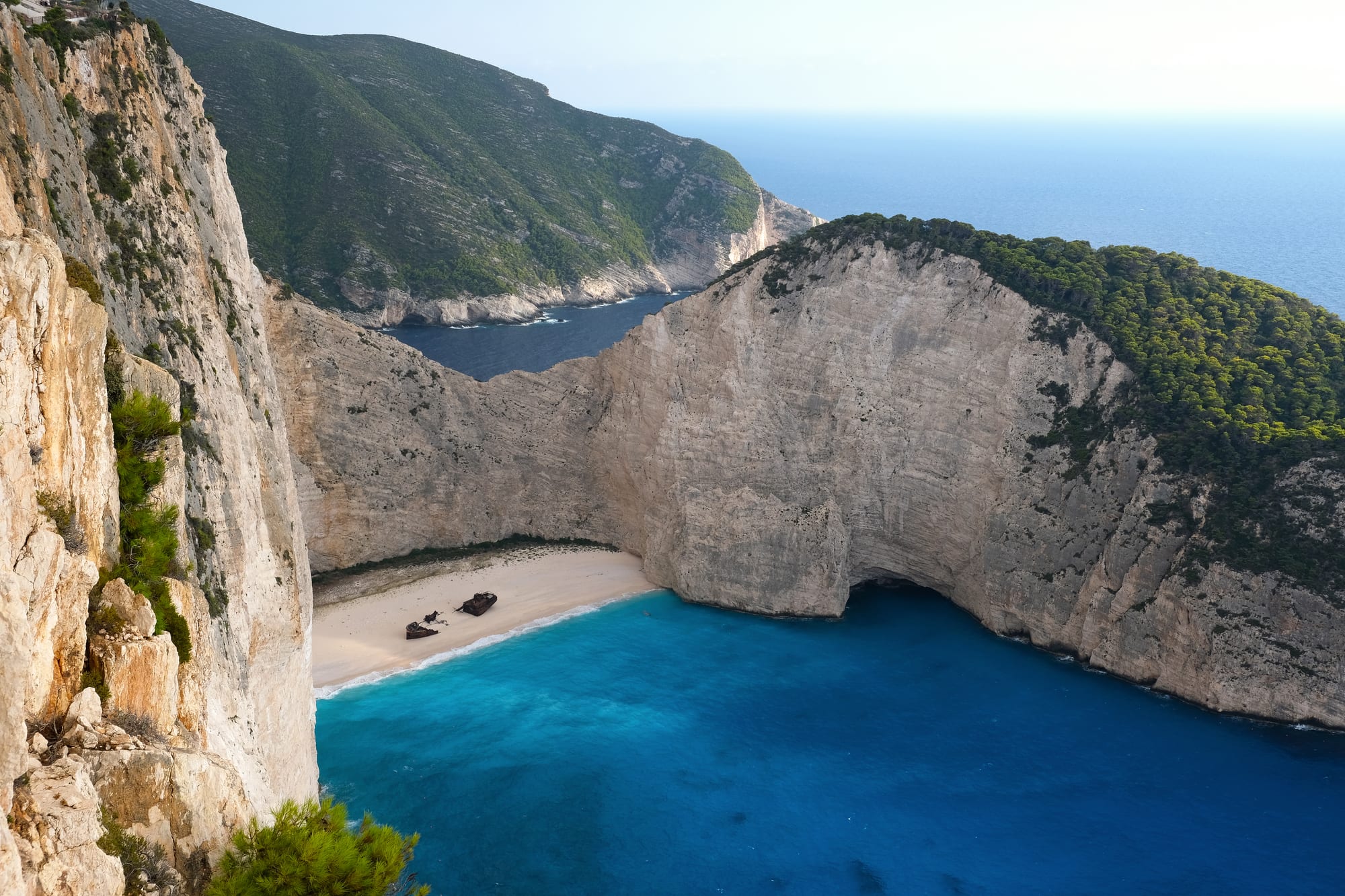 A rusting shipwreck on a white-sand cove enclosed by tall white cliffs and turquoise water