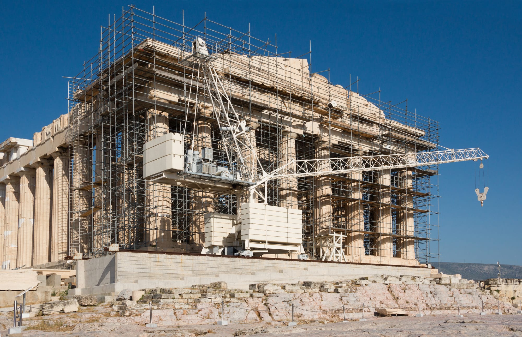 The columned facade of a marble temple with scaffolding and restoration cranes