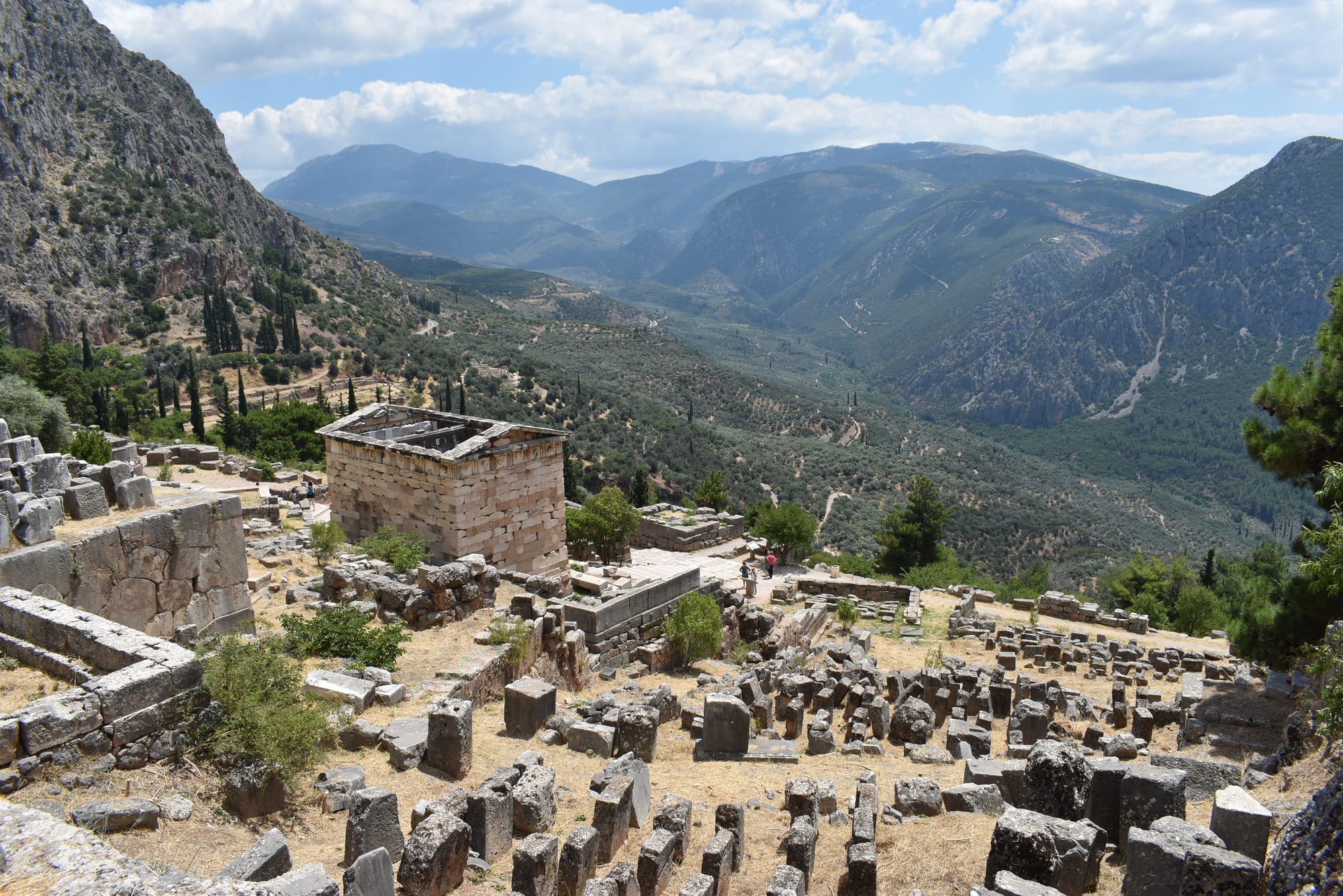 Ruined temple columns and terraces on a steep mountainside above a valley of olive trees