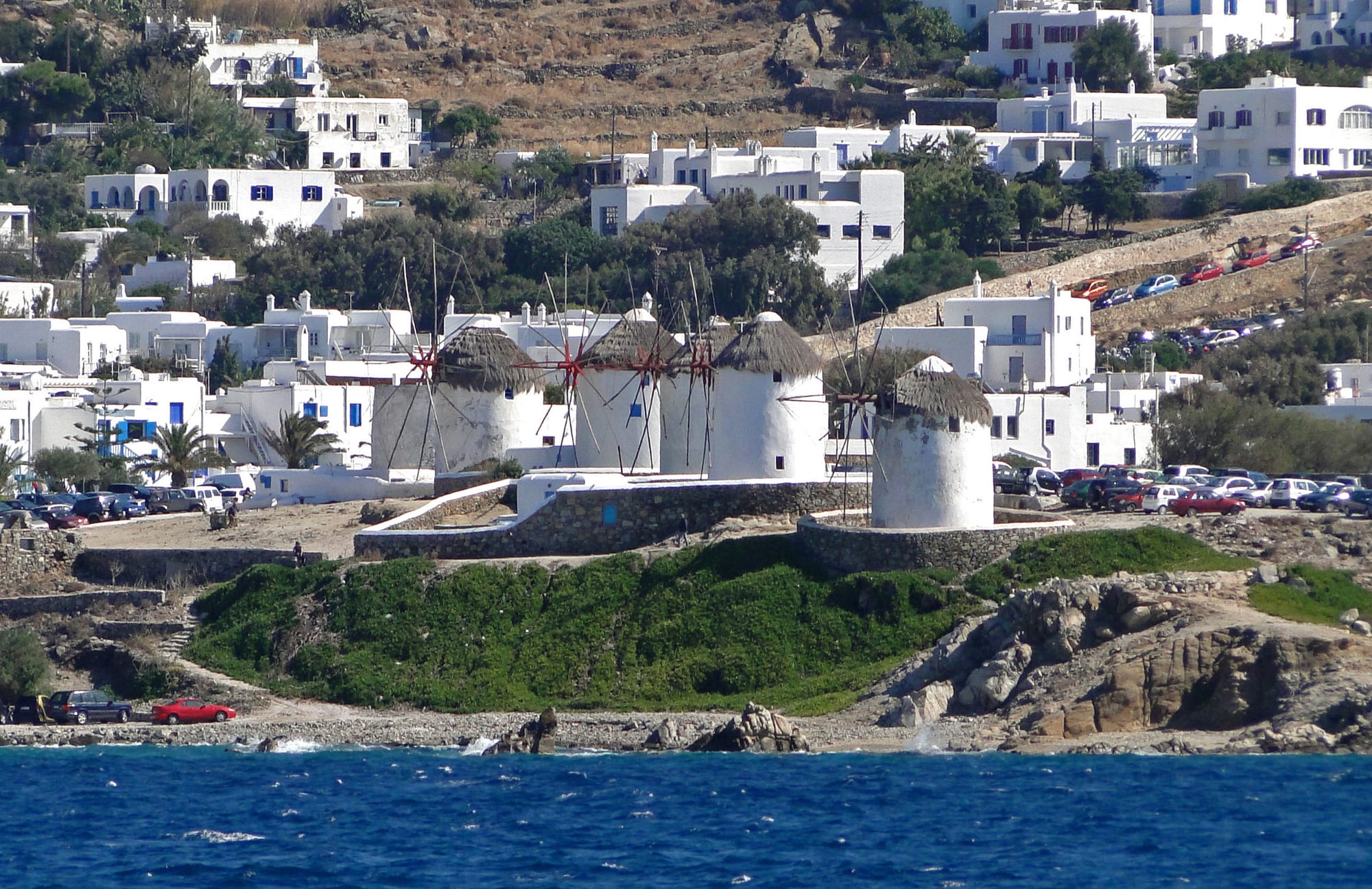 A row of round white windmills with thatched conical roofs above a bay