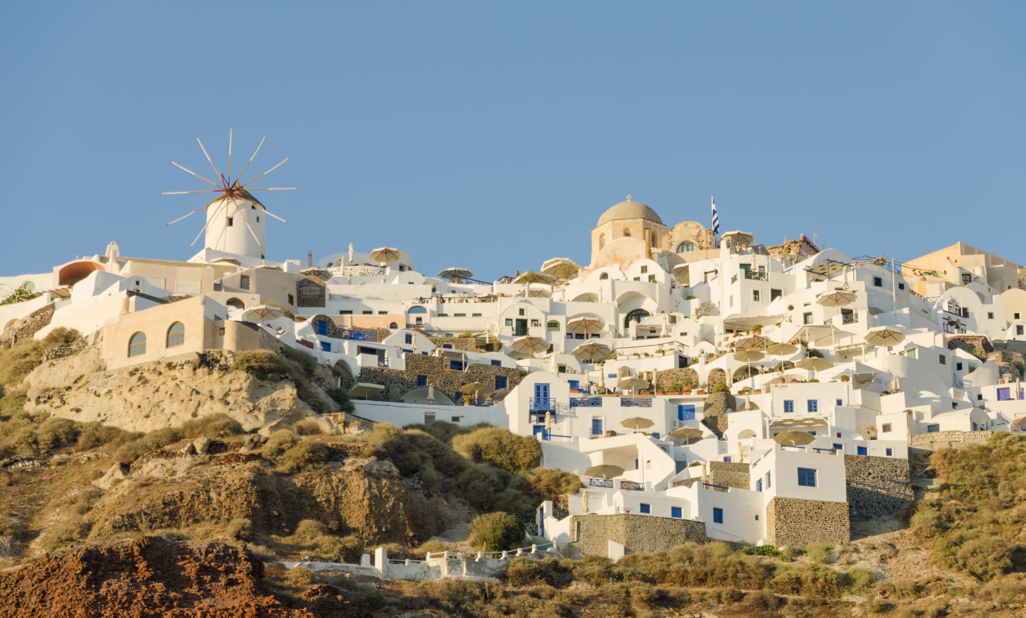 White cube houses and blue domes stacked on a cliff high above a dark blue sea