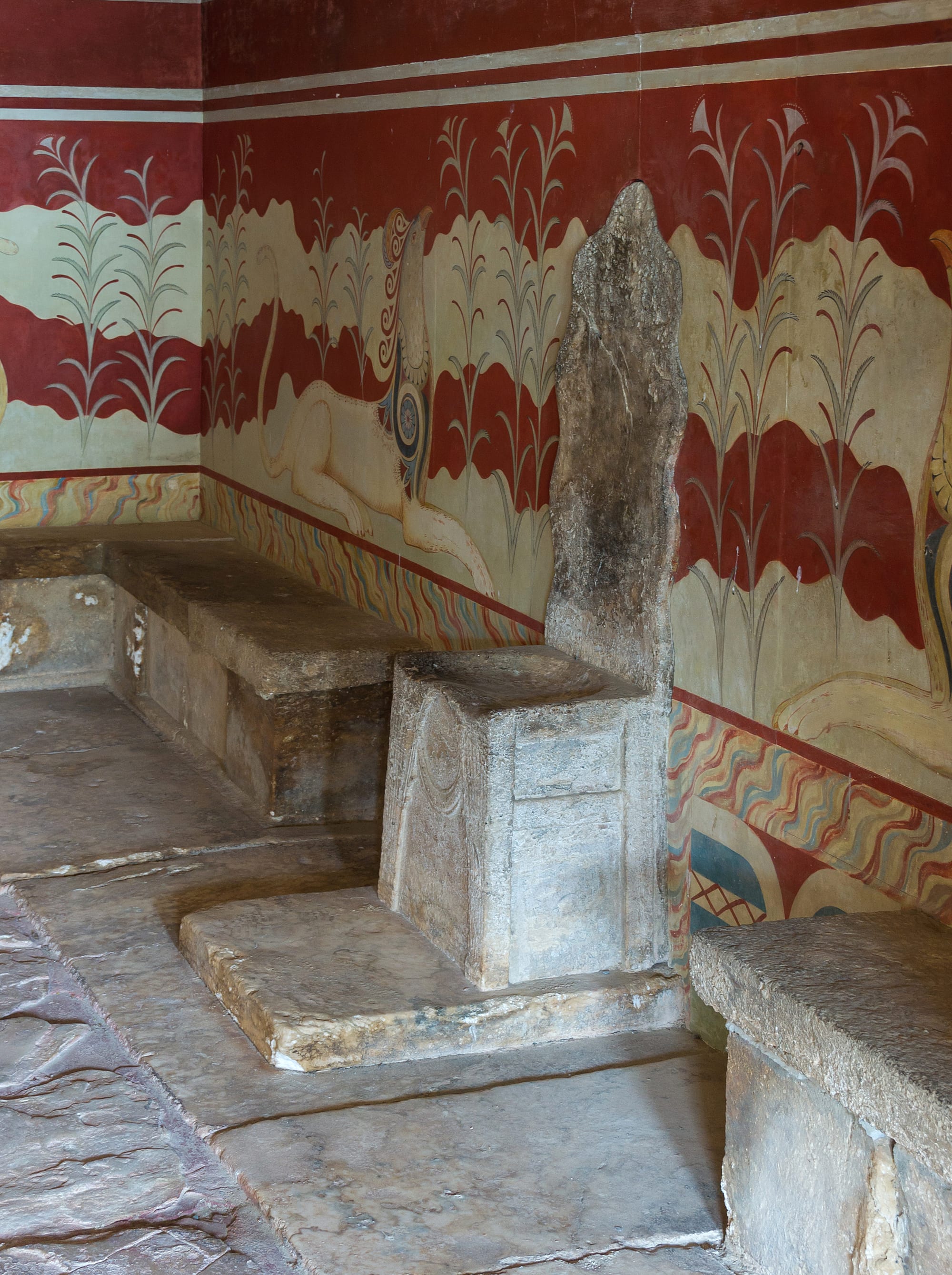 A stone throne set against a wall painted with griffins in a small chamber at Knossos