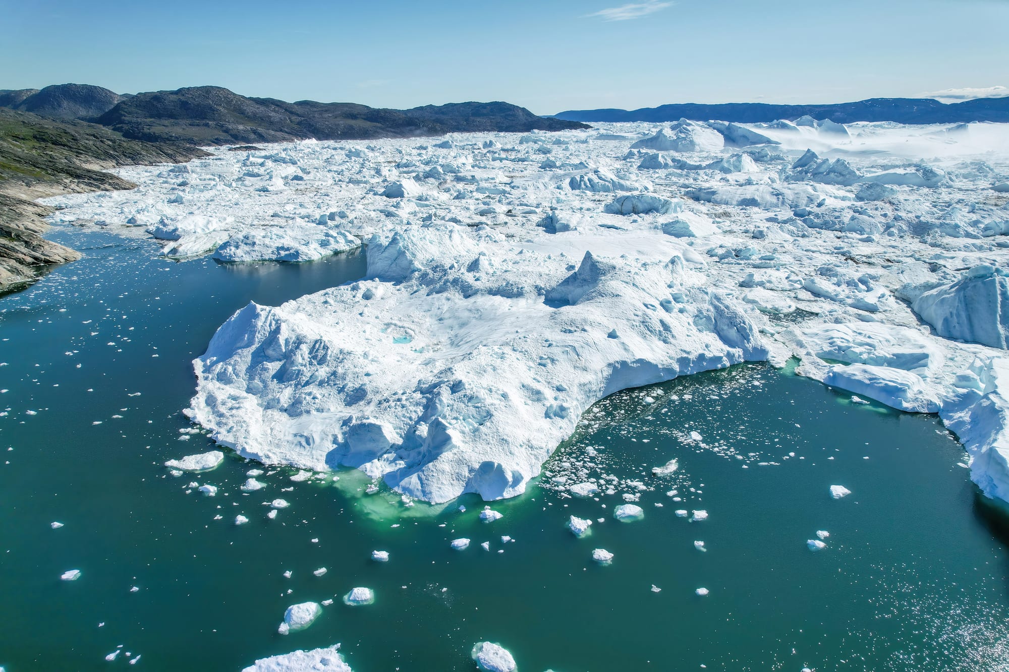 An aerial view of a glacier front breaking into a bay filled with broken ice