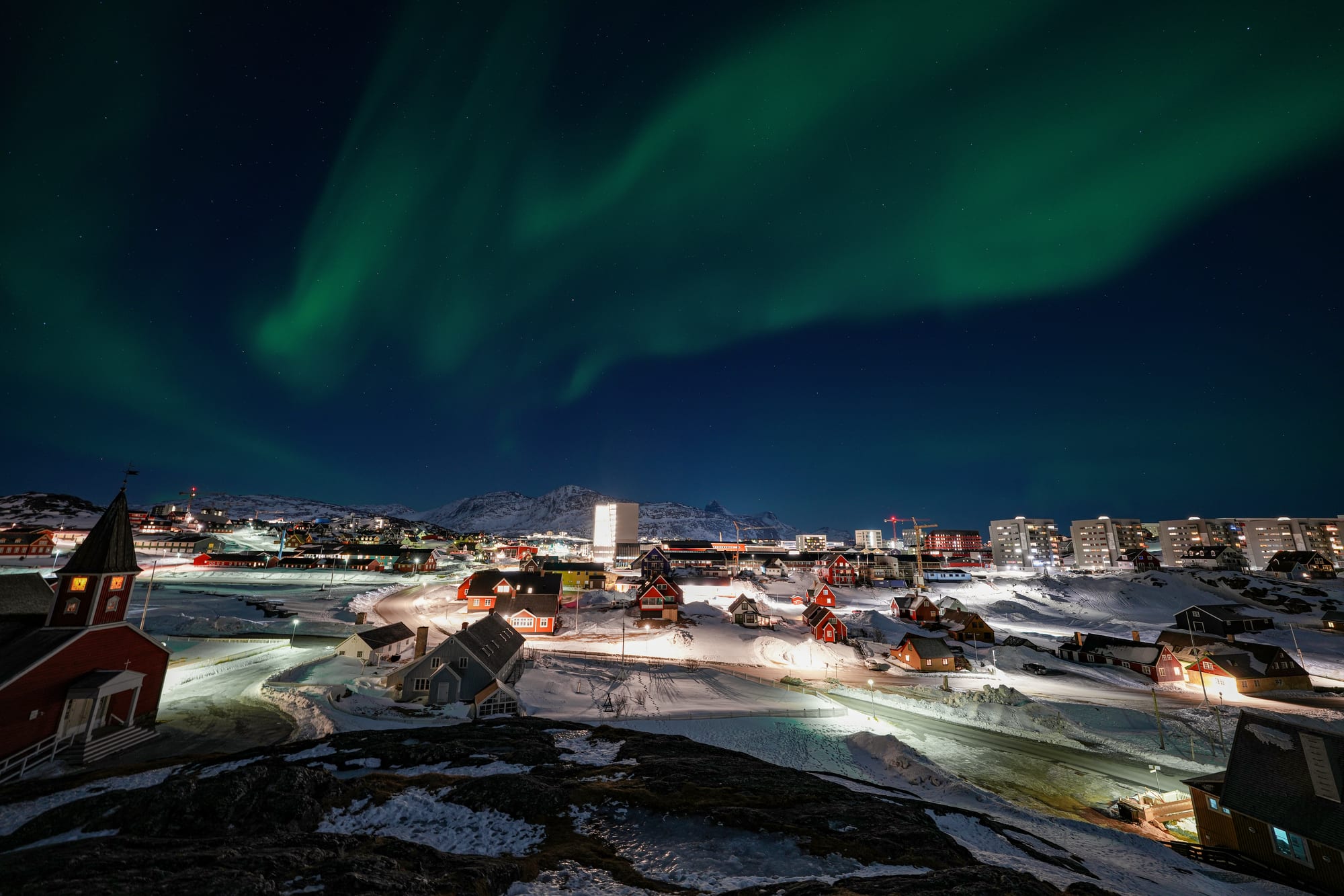 A small city of low buildings and apartment blocks under green aurora
