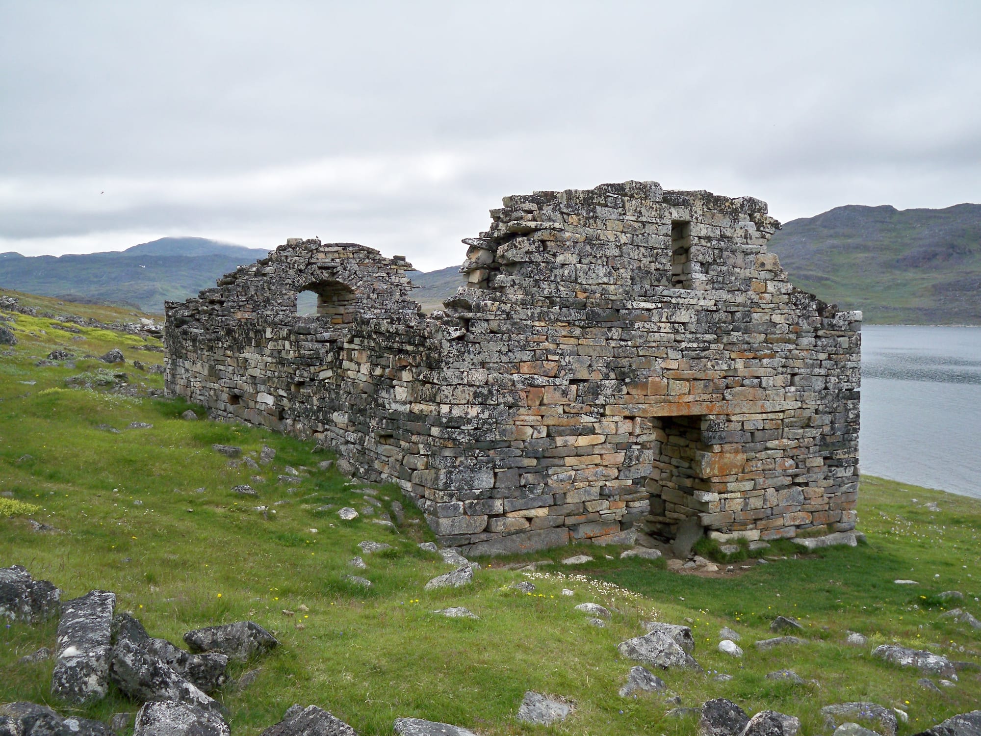 Roofless stone church walls standing in a green meadow above a fjord
