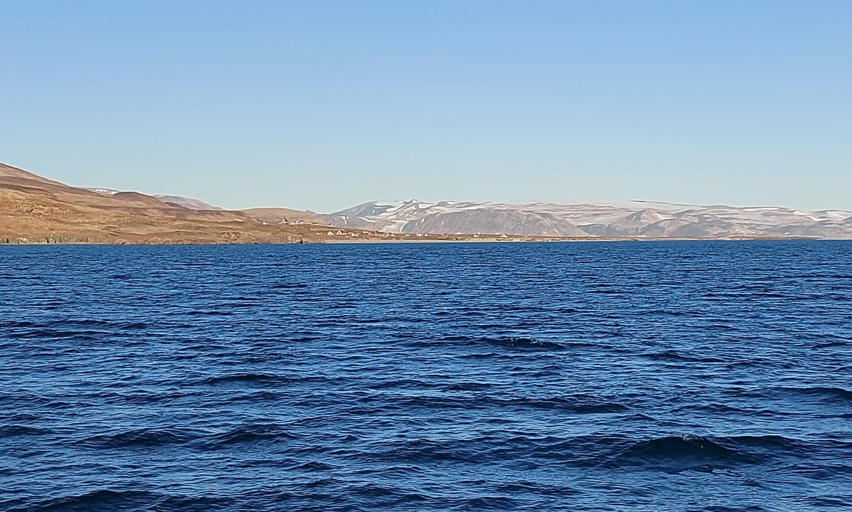 A wide fjord with tabular icebergs and bare reddish mountains under low light