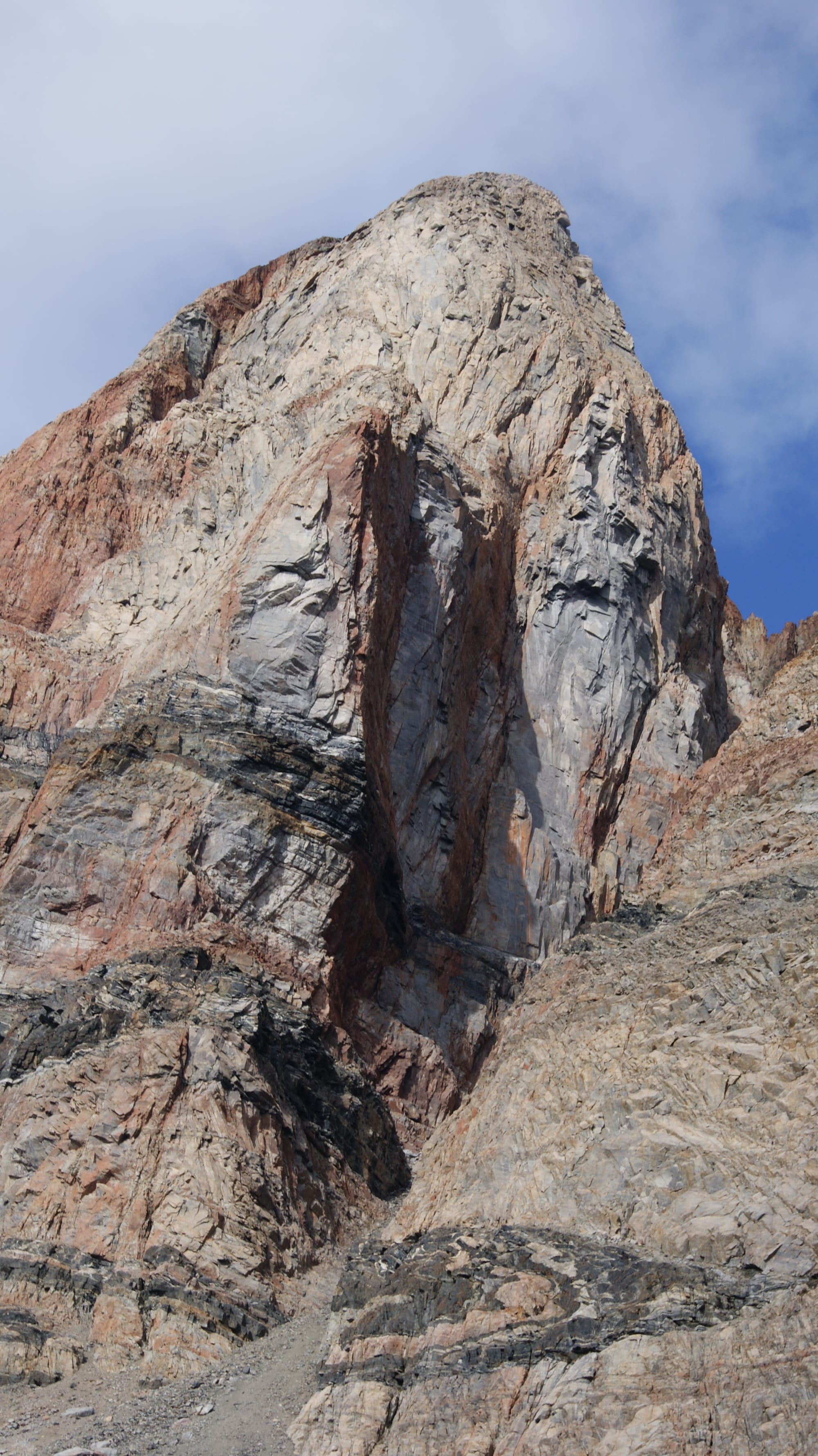 A steep heart-shaped mountain of dark rock rising above a small settlement and sea ice
