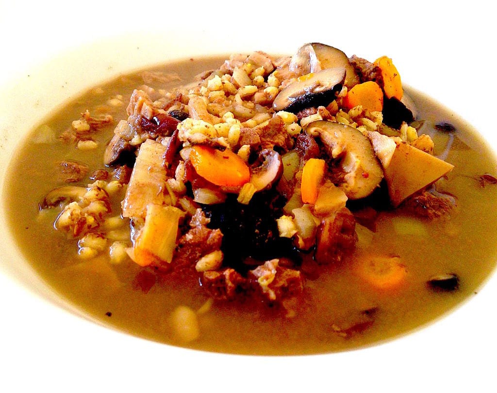 A bowl of pale broth with pieces of meat and potato