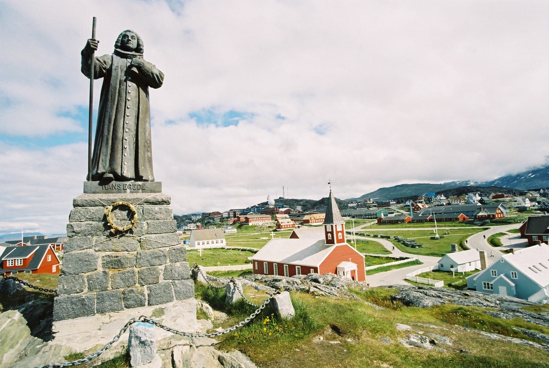 A bronze statue of Hans Egede in clerical robes on a tall stone plinth on a hill above Nuuk