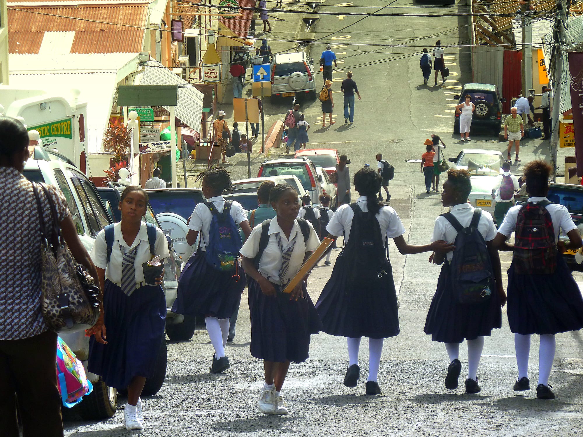 Uniformed schoolgirls walking down a busy street in St George's past parked cars and shops