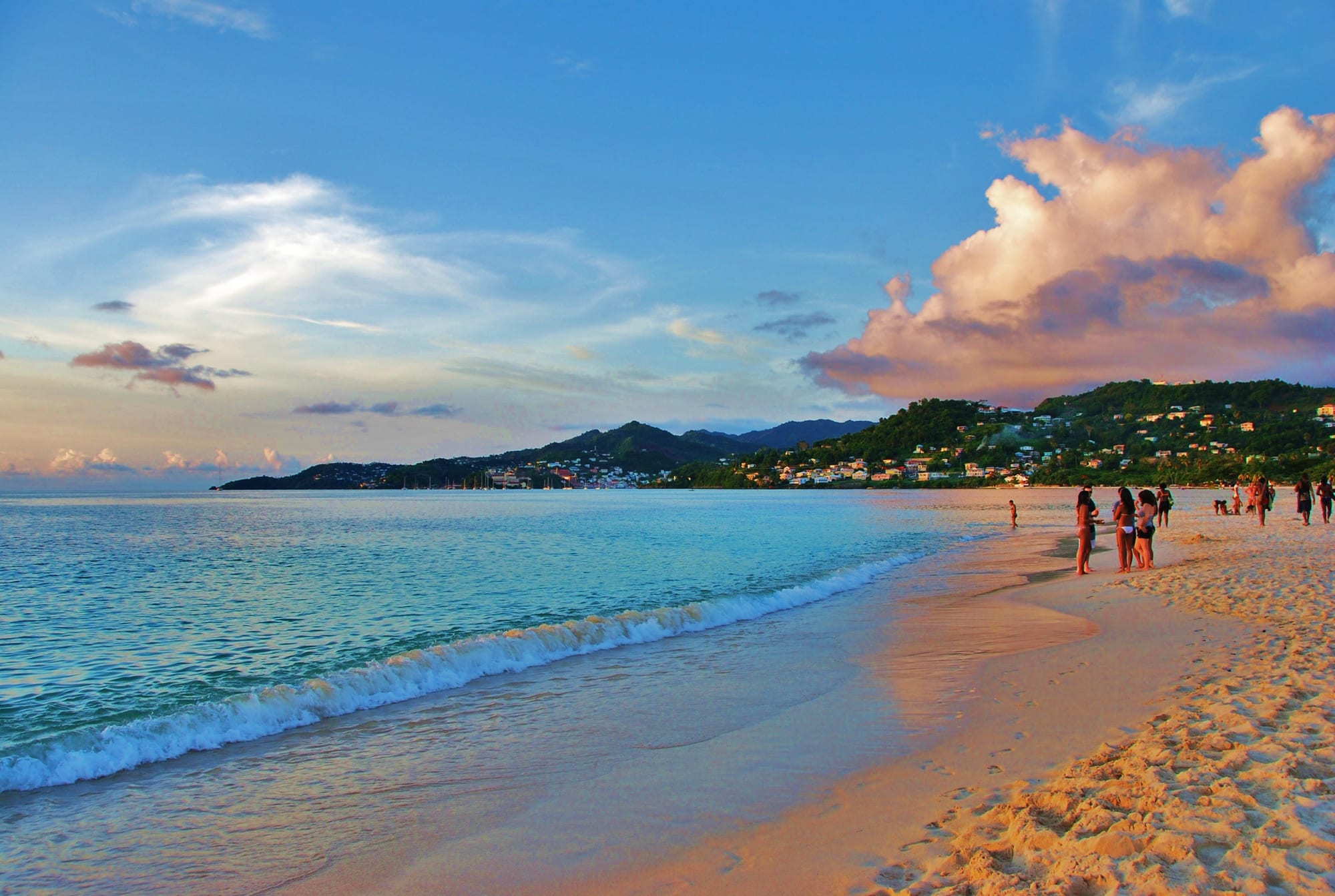 A long curve of pale sand meeting calm turquoise water, green hills behind