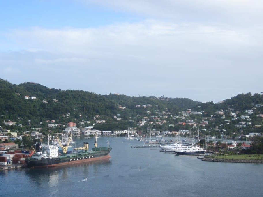 A curved harbour lined with red-roofed colonial buildings rising up a green hillside