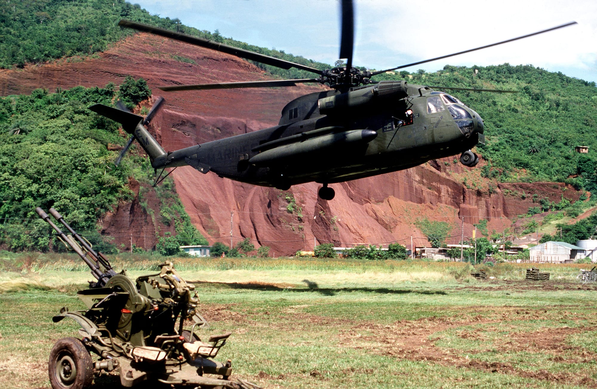 A large US military helicopter flying low over Grenada's green hills in October 1983