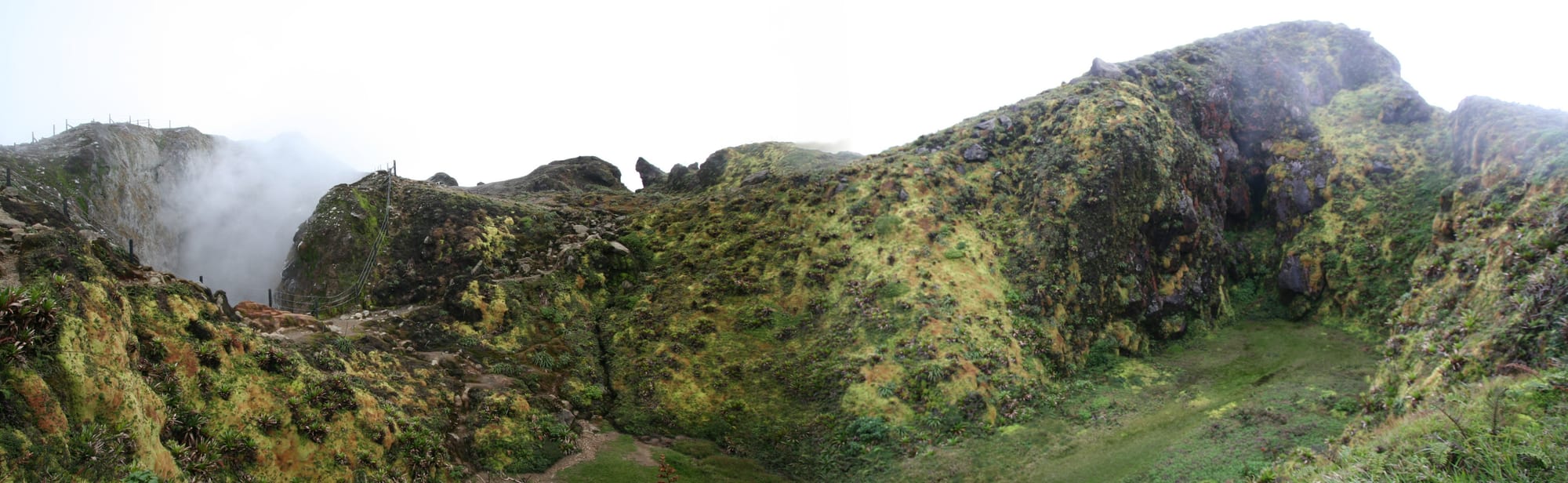 A misty volcanic summit of dark rock and steaming vents under a grey sky