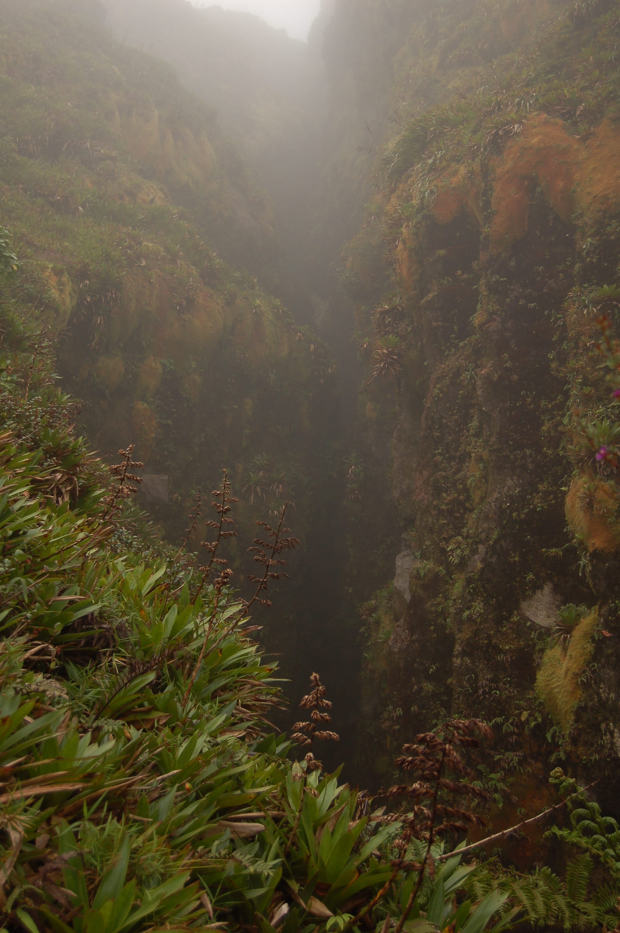 A deep steaming fissure splitting bare volcanic rock on a cloudy summit