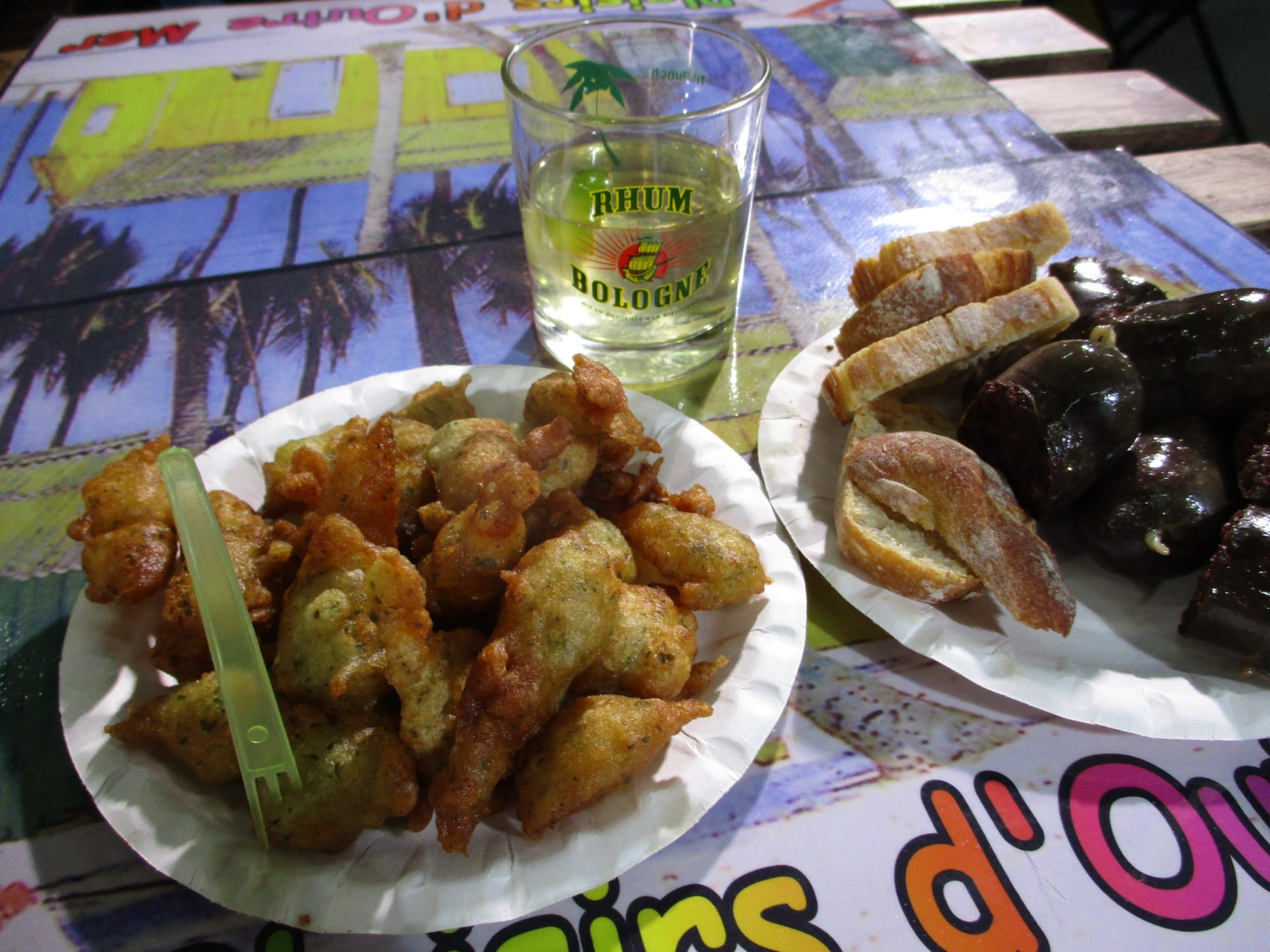 Fried fritters, sliced sausage and a small glass of rum drink on a table