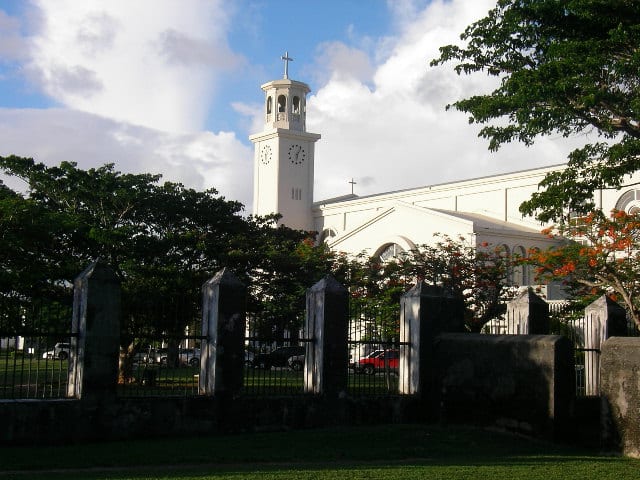 A grassy plaza with a stone arch and colonial-era ruins under palm trees