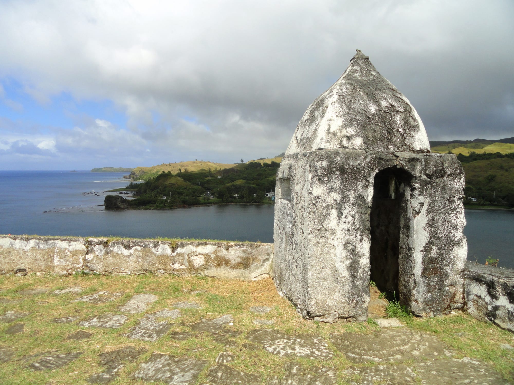 A small restored Spanish fort with a cannon on a green headland above a bay