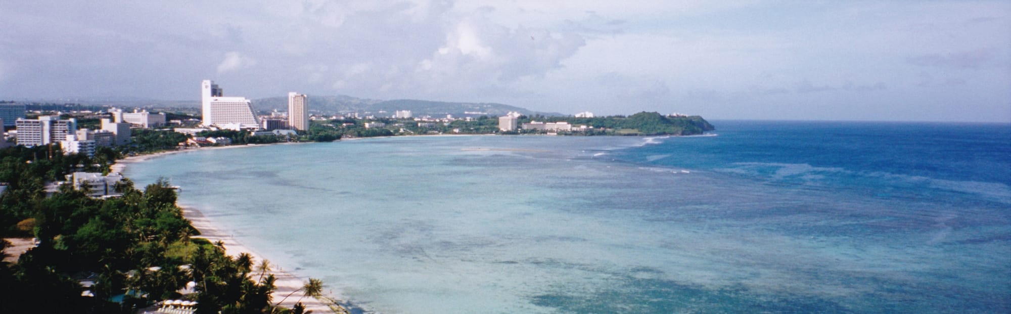 A wide reef flat of shallow blue water at low tide with hotels along the shore