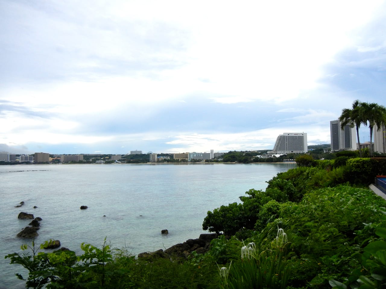 A curving bay of pale turquoise water and reef backed by hotels and green hills