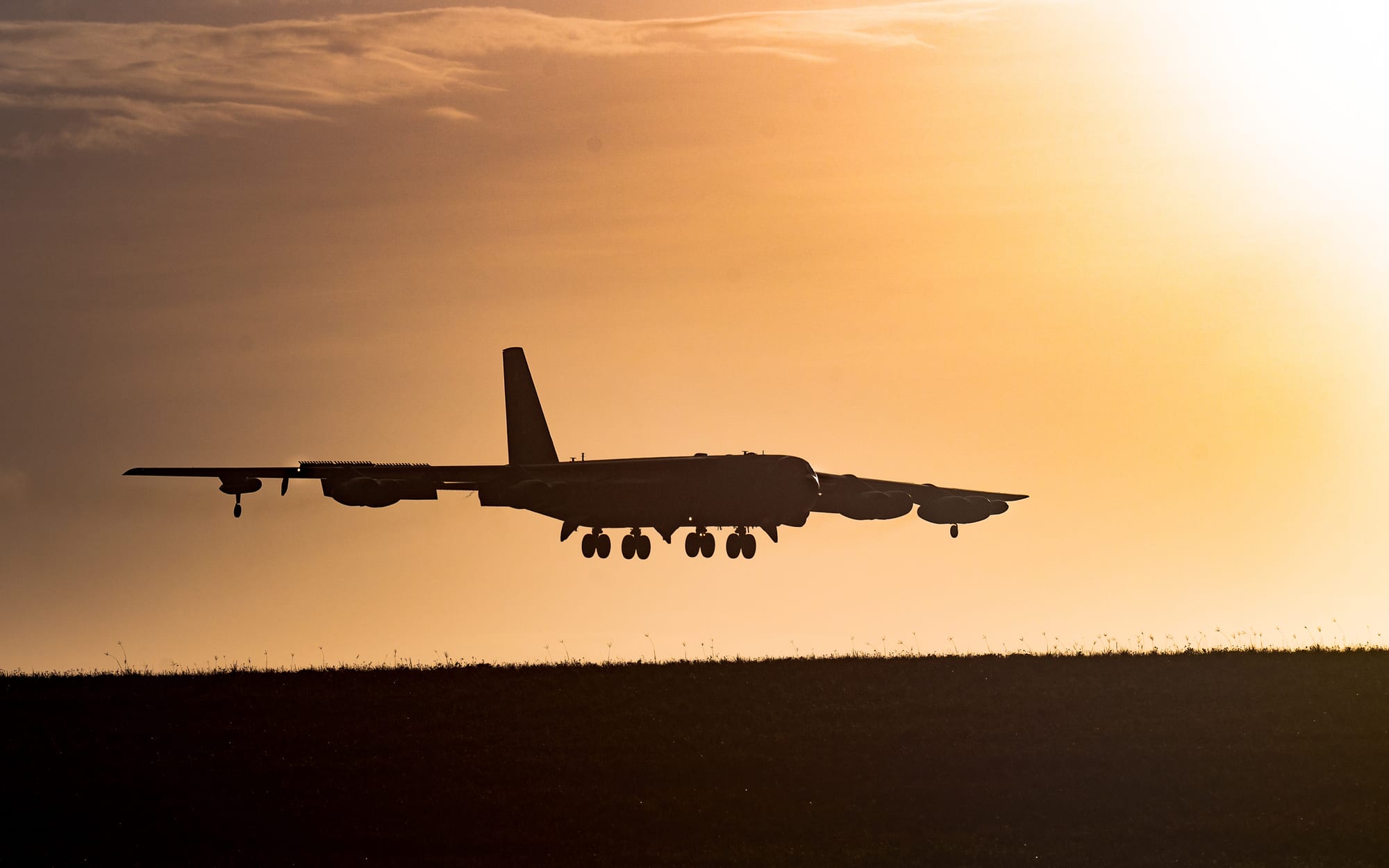 A large grey B-52 bomber on approach to a runway with jungle beyond