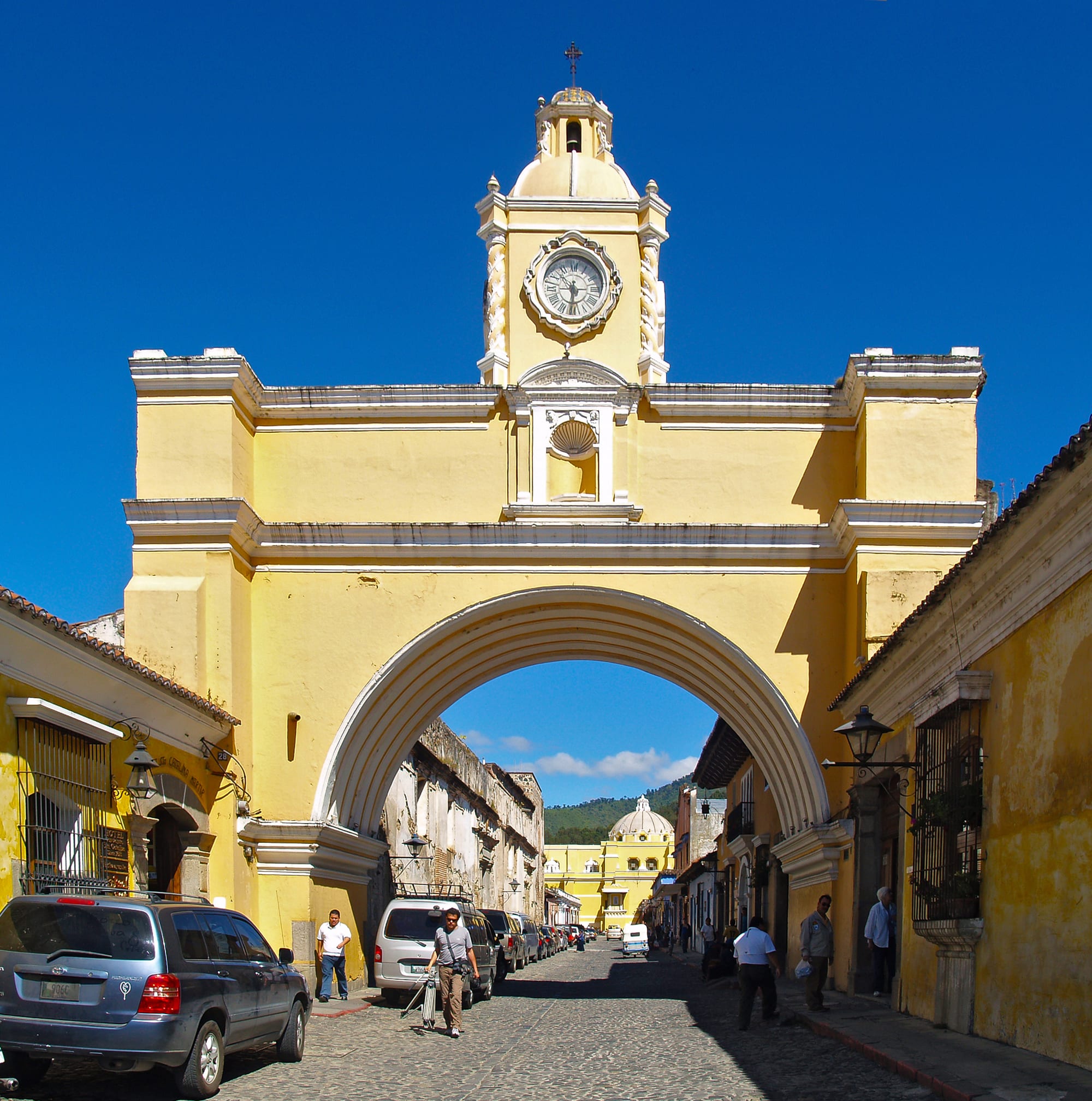 A yellow colonial archway over a cobbled street with a volcano framed beyond it