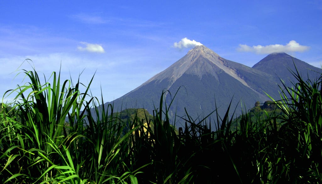 Two large volcanic cones side by side, one puffing a plume of ash