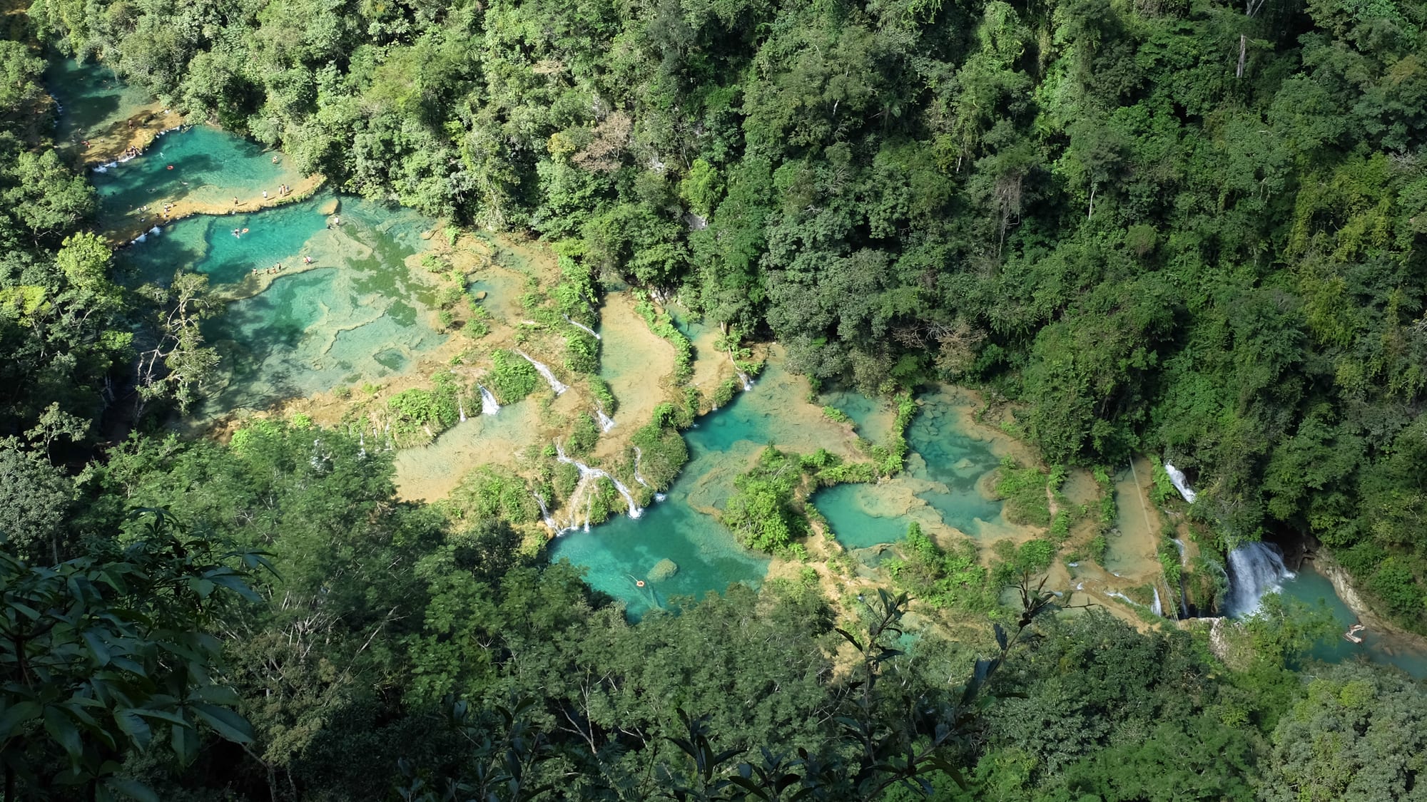 A staircase of turquoise natural pools on a limestone bridge over a river, in jungle