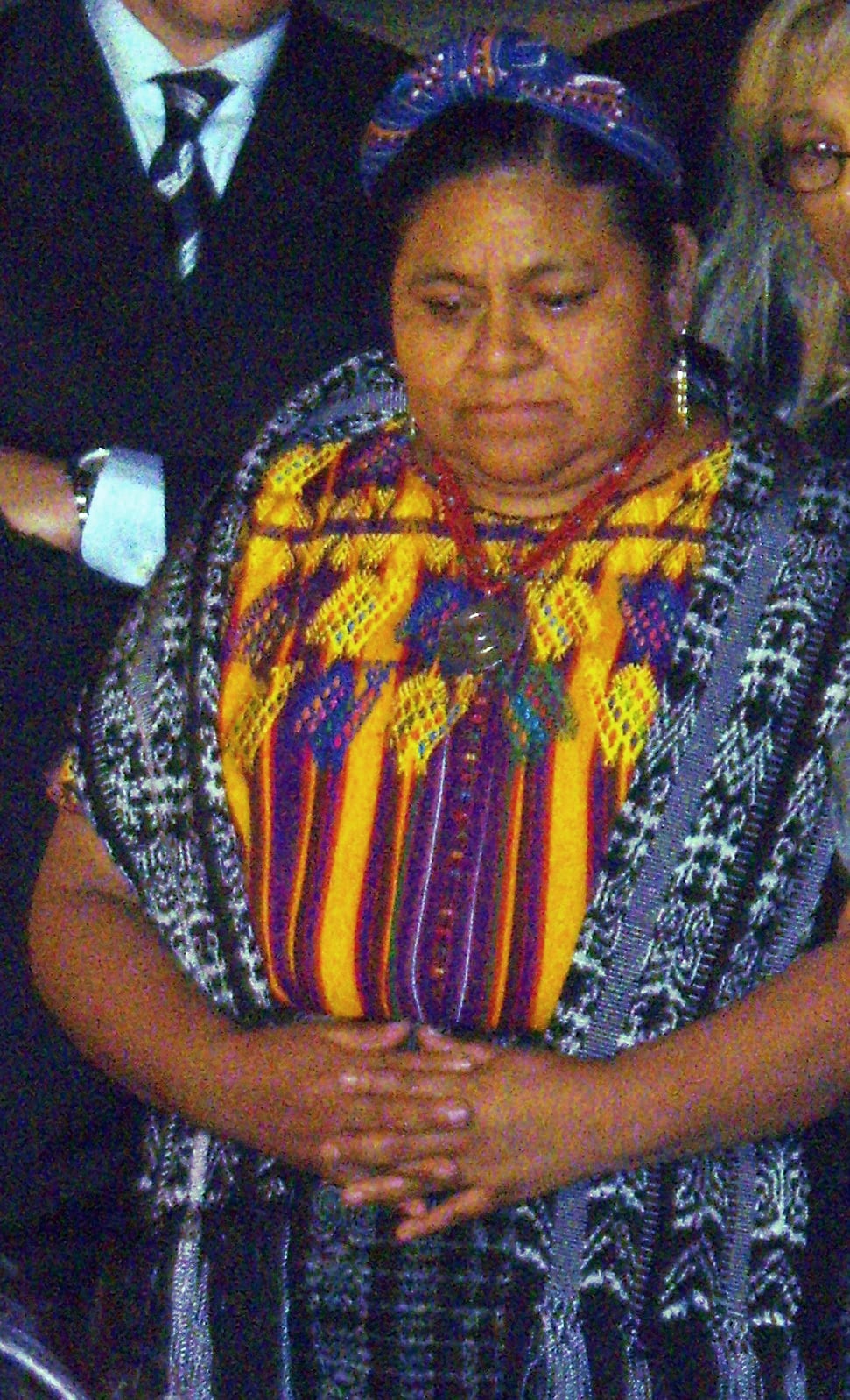 Rigoberta Menchú in traditional K'iche' dress speaking at a podium