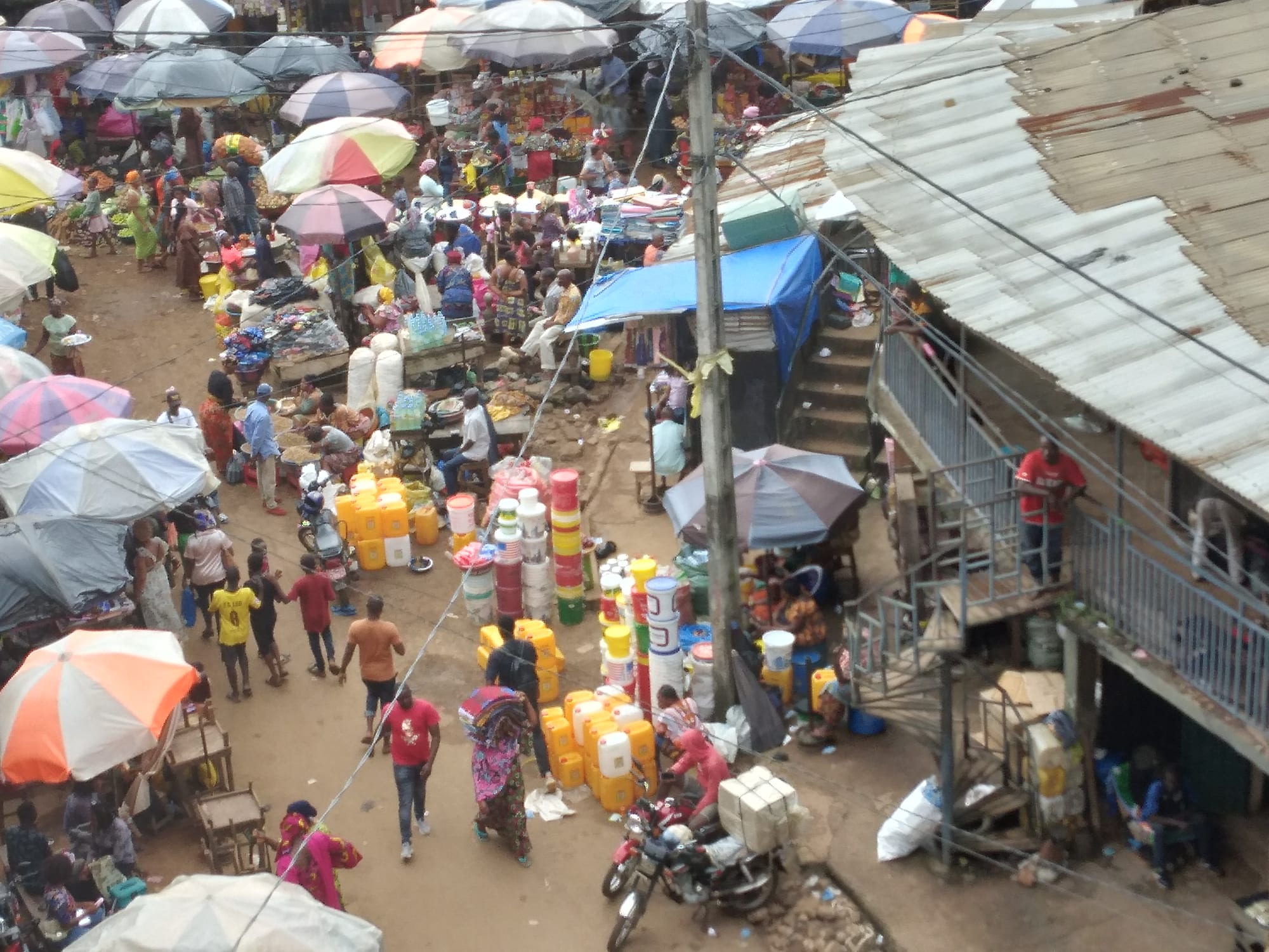 An aerial view of a crowded market with many umbrellas, stalls of goods, and people moving through narrow lanes