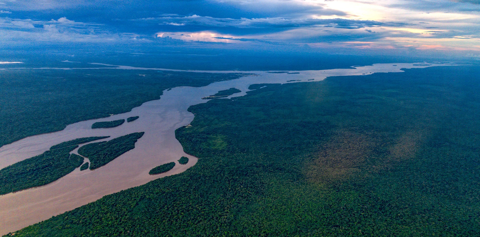A wide muddy river winding through unbroken rainforest, seen from the air