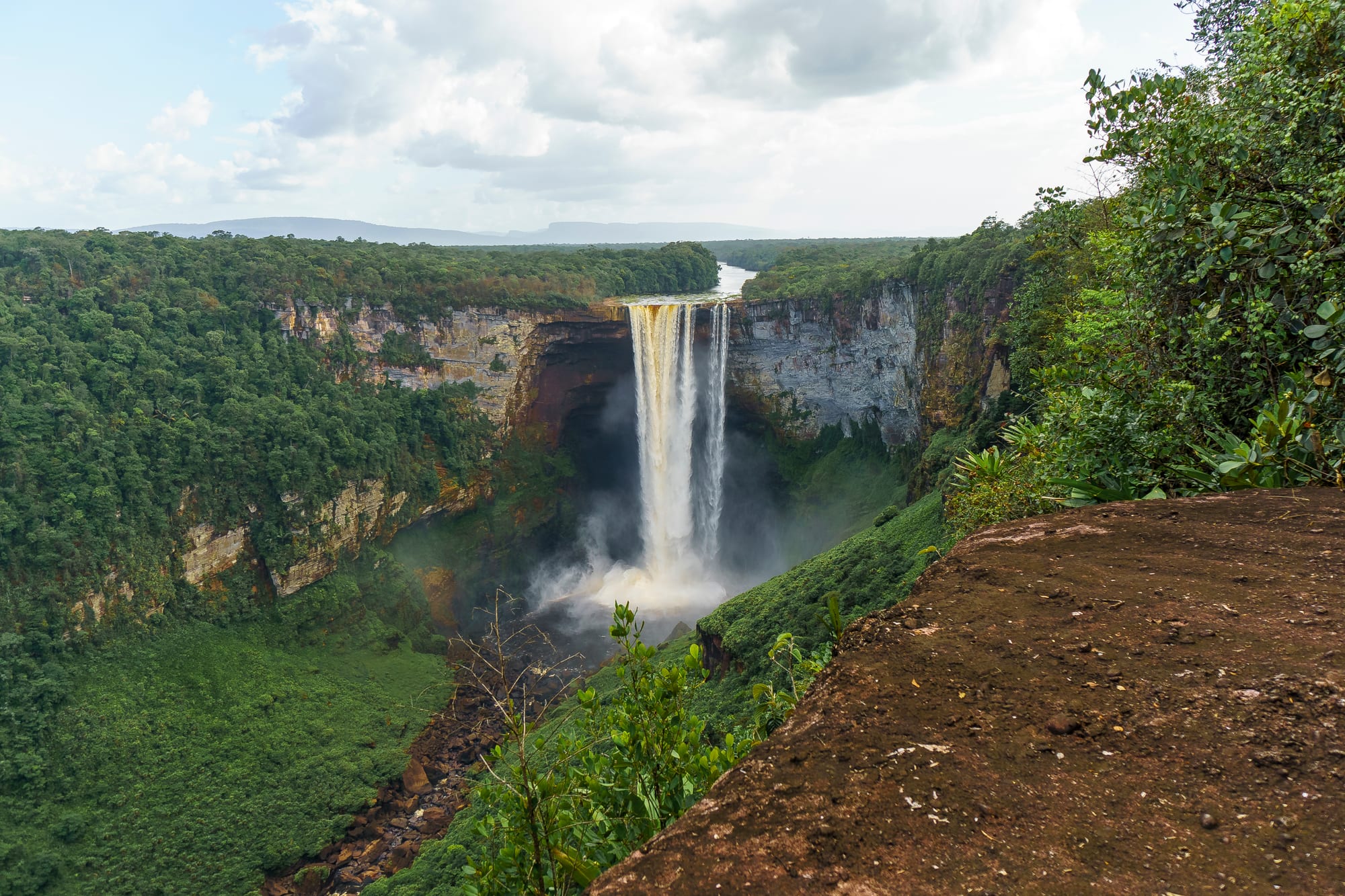 A massive single-drop waterfall plunging off a forested tabletop cliff into a gorge