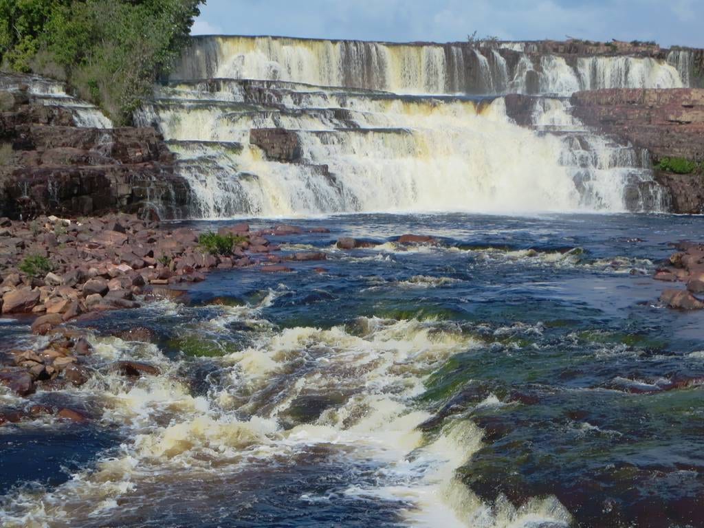 A river spilling in wide, low steps over dark terraced rock in open country