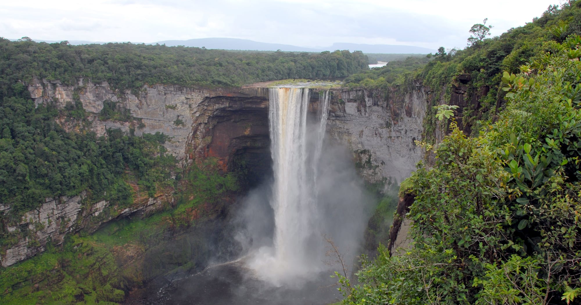 A broad brown river pouring over a sheer cliff edge with rainforest all around