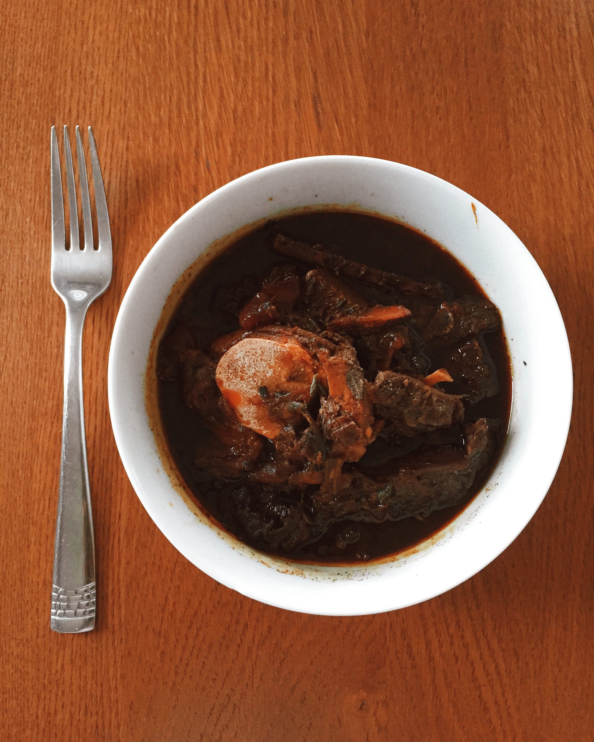 A dark, thick stew with visible pieces of meat in a bowl