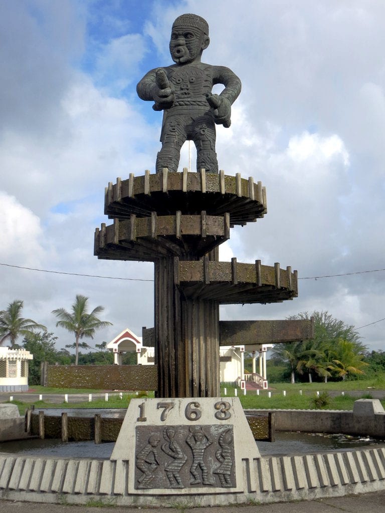 A tall bronze statue of a defiant male figure on a plinth in a Georgetown plaza