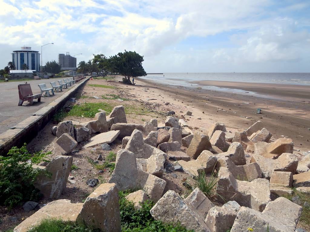 A stretch of the Georgetown sea wall with benches, concrete sea-defence blocks, and the wide Atlantic beach beyond