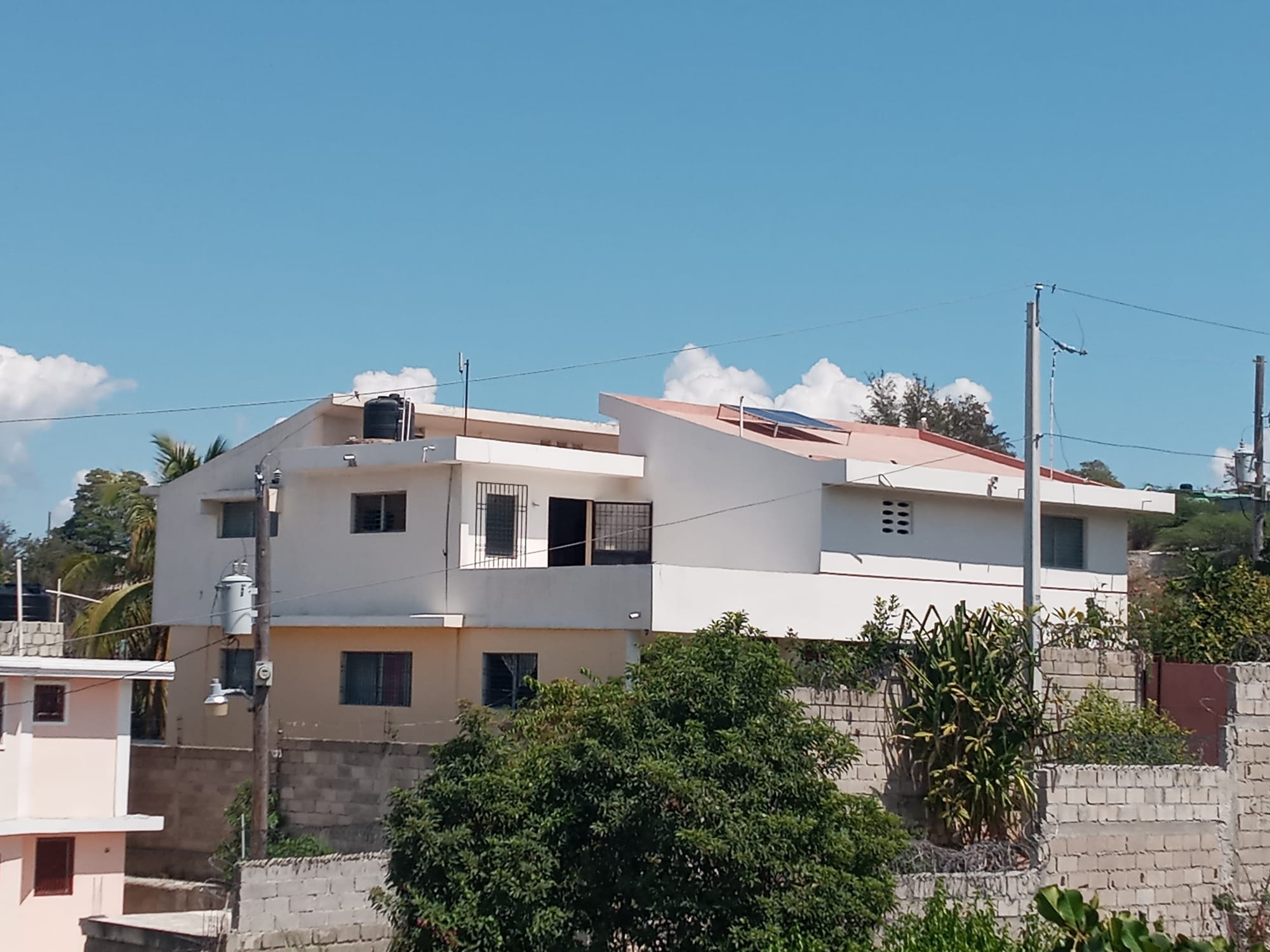 A multi-storey house with a water tank and solar panel on the roof, behind a concrete block wall, in the Delmas area of Port-au-Prince