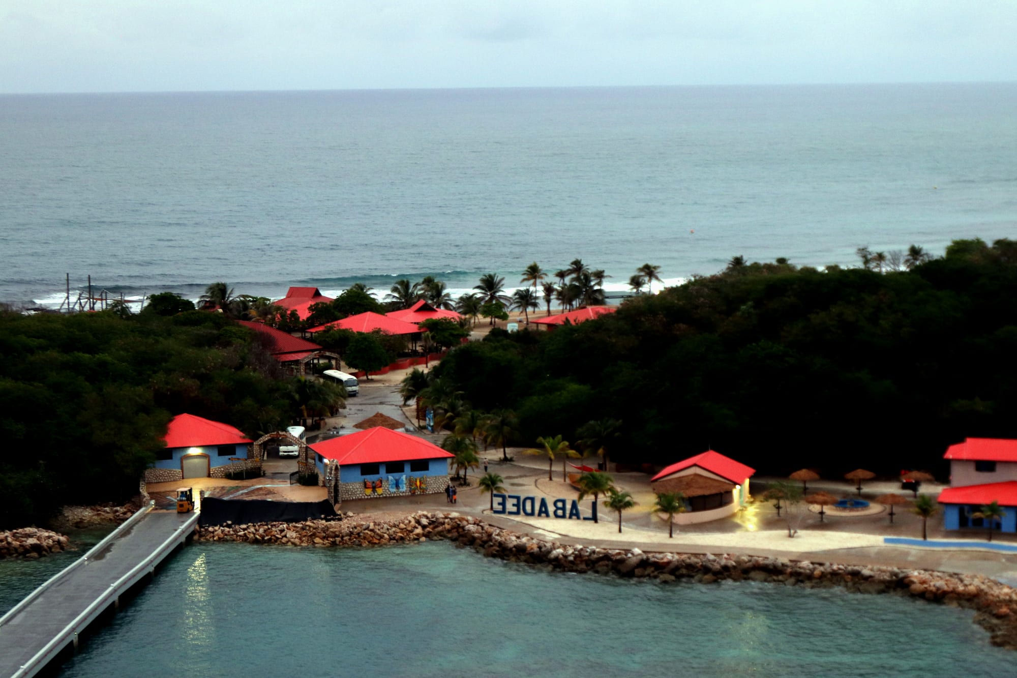 An aerial view of a palm-lined beach resort with red roofs beside turquoise water