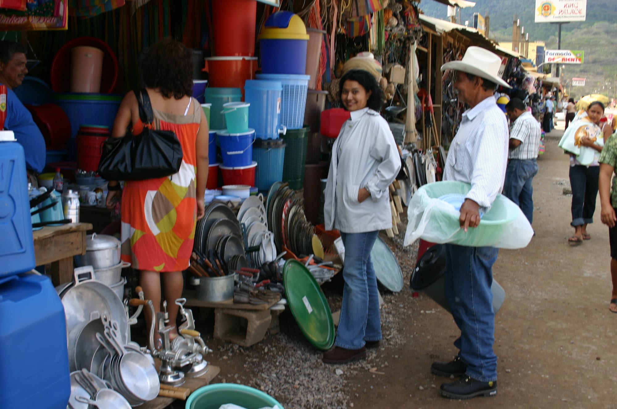 An open-air market street in Catacamas, Honduras, with vendors selling pots, pans and plastic goods and shoppers browsing