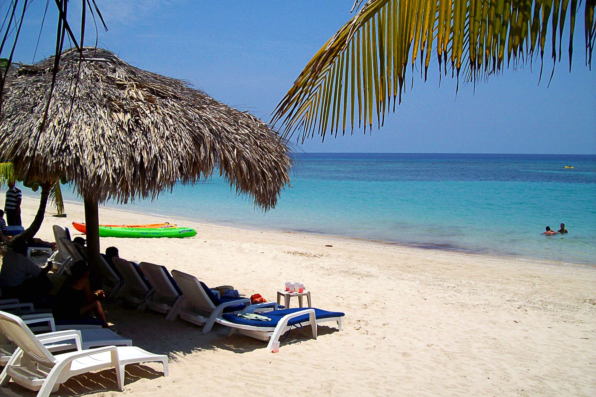 A palm-lined white beach with clear shallow water and a reef line offshore