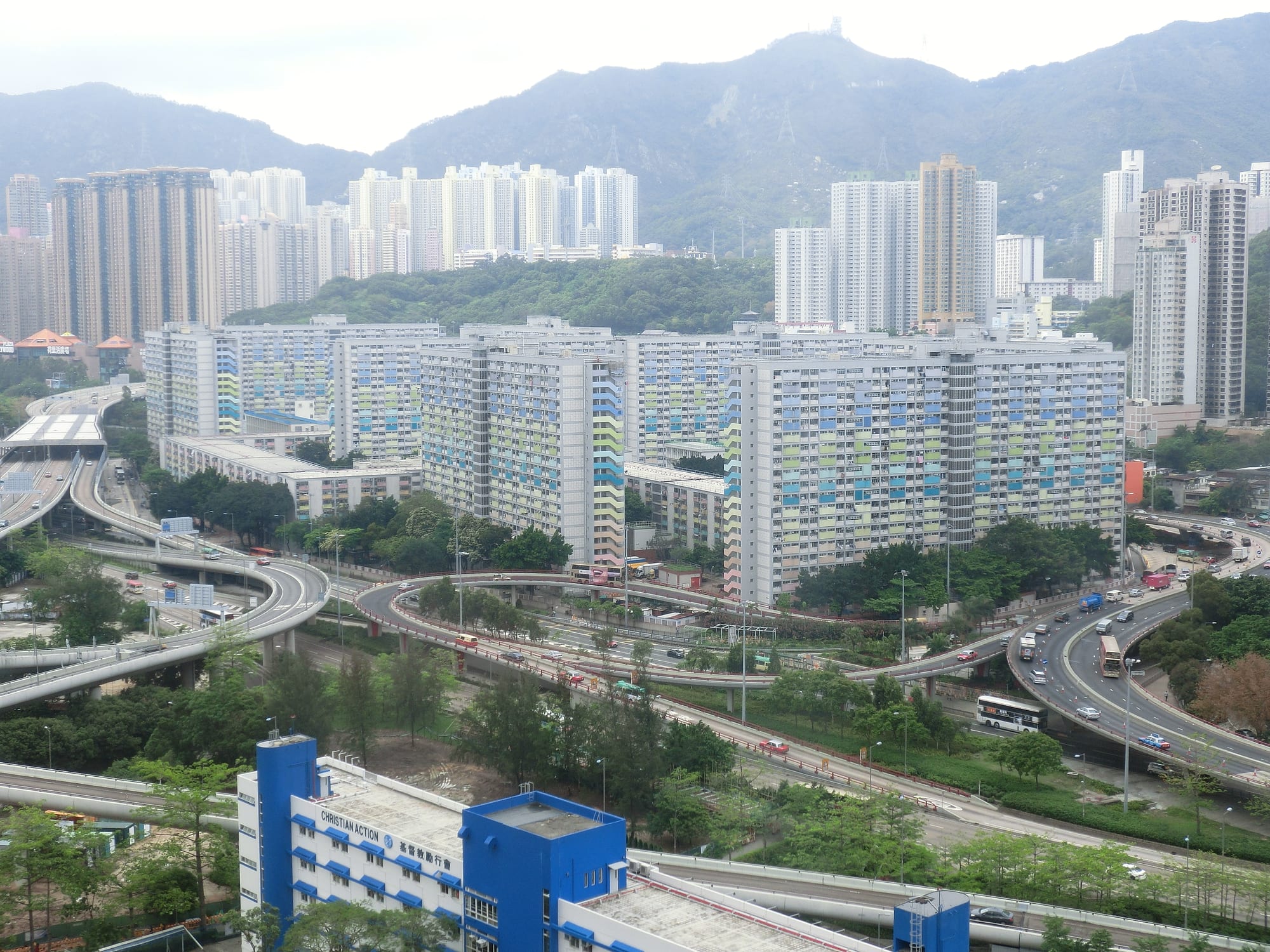 Rows of pastel-coloured public housing tower blocks at Choi Hung Estate, with mountains behind and a highway interchange below