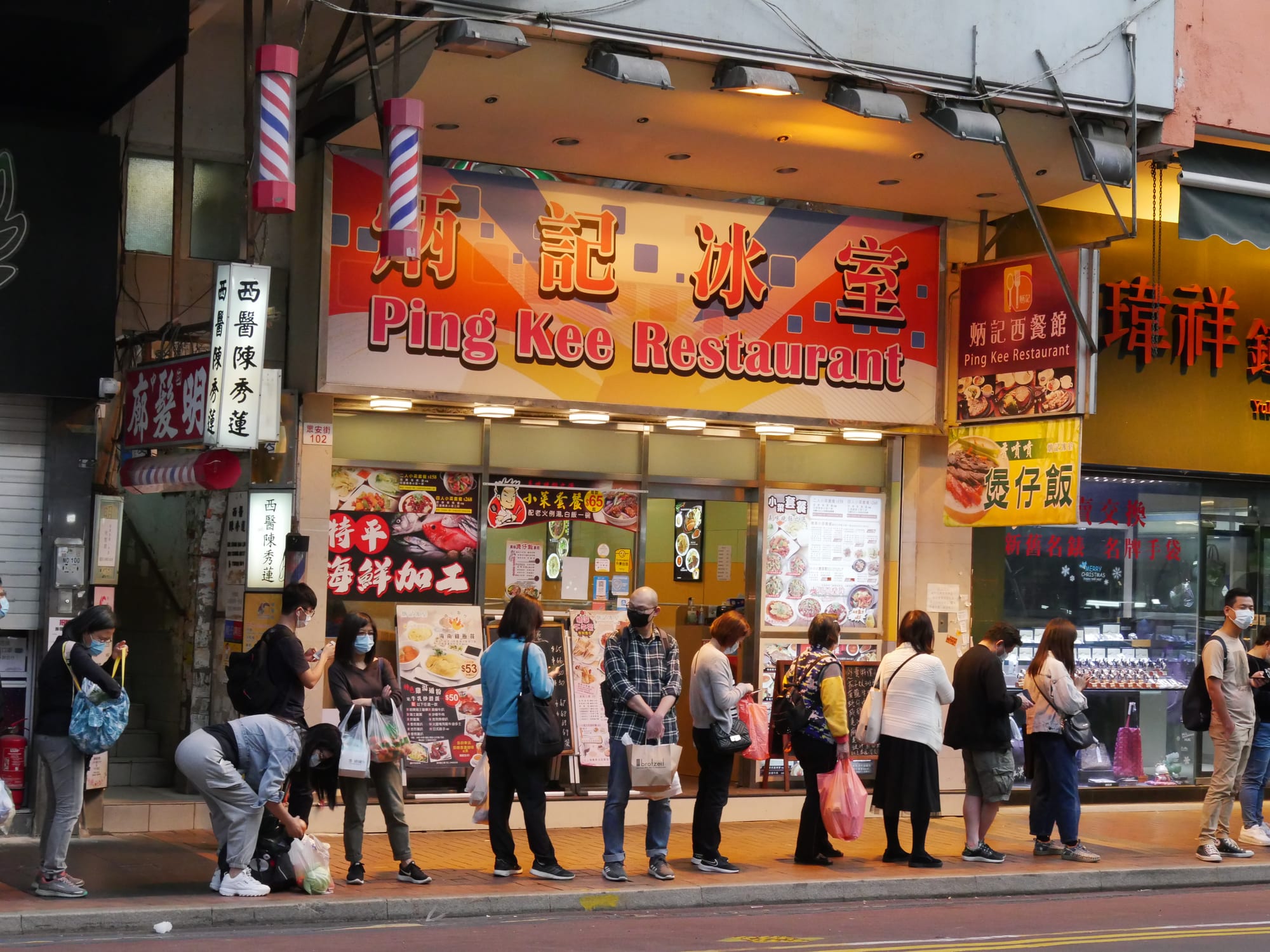 A queue of people waiting outside Ping Kee Restaurant, a cha chaan teng tea restaurant, under its illuminated sign in Tsuen Wan