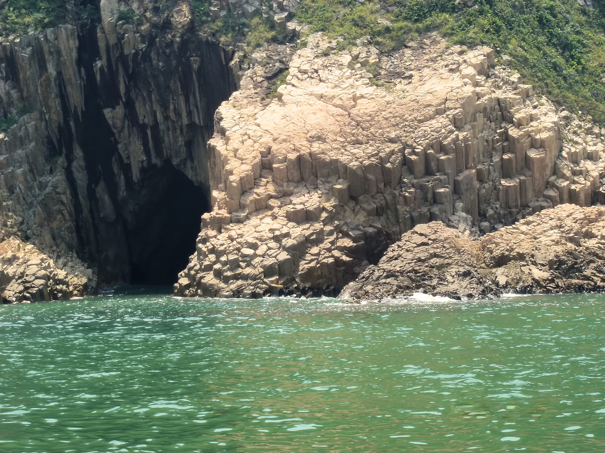 Tall hexagonal rock columns rising in a curtain from the sea at the base of a cliff