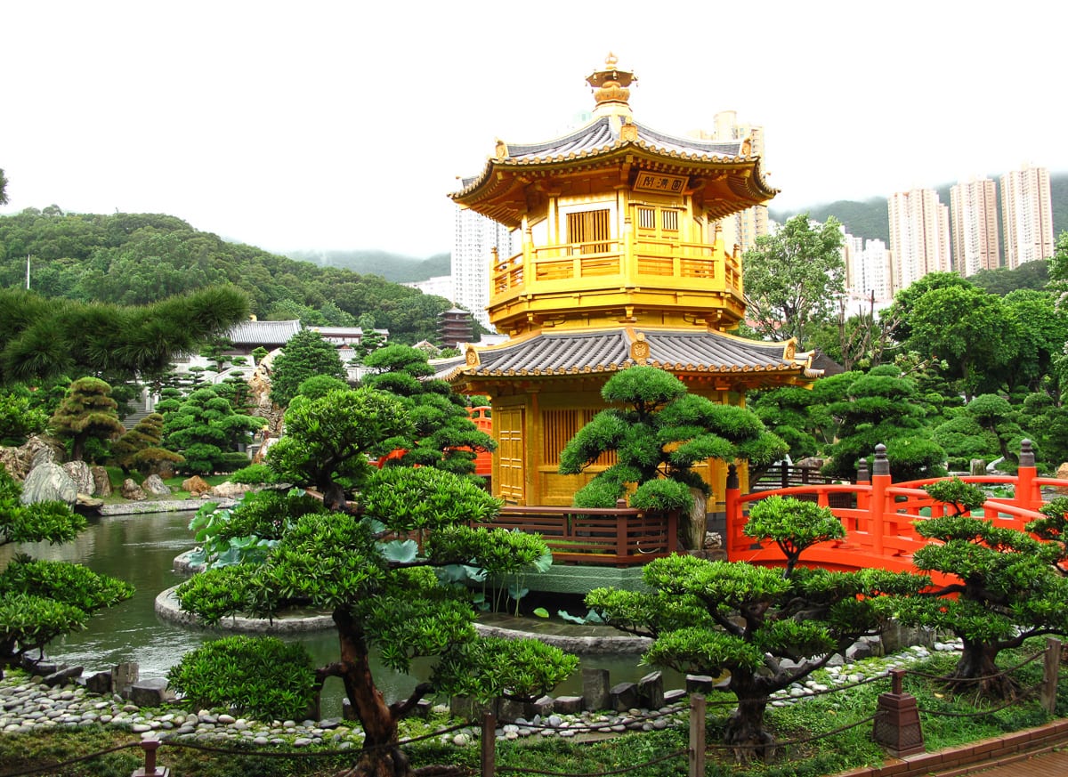 A classical Chinese garden with a golden pavilion on a pond, framed by trees and rockeries