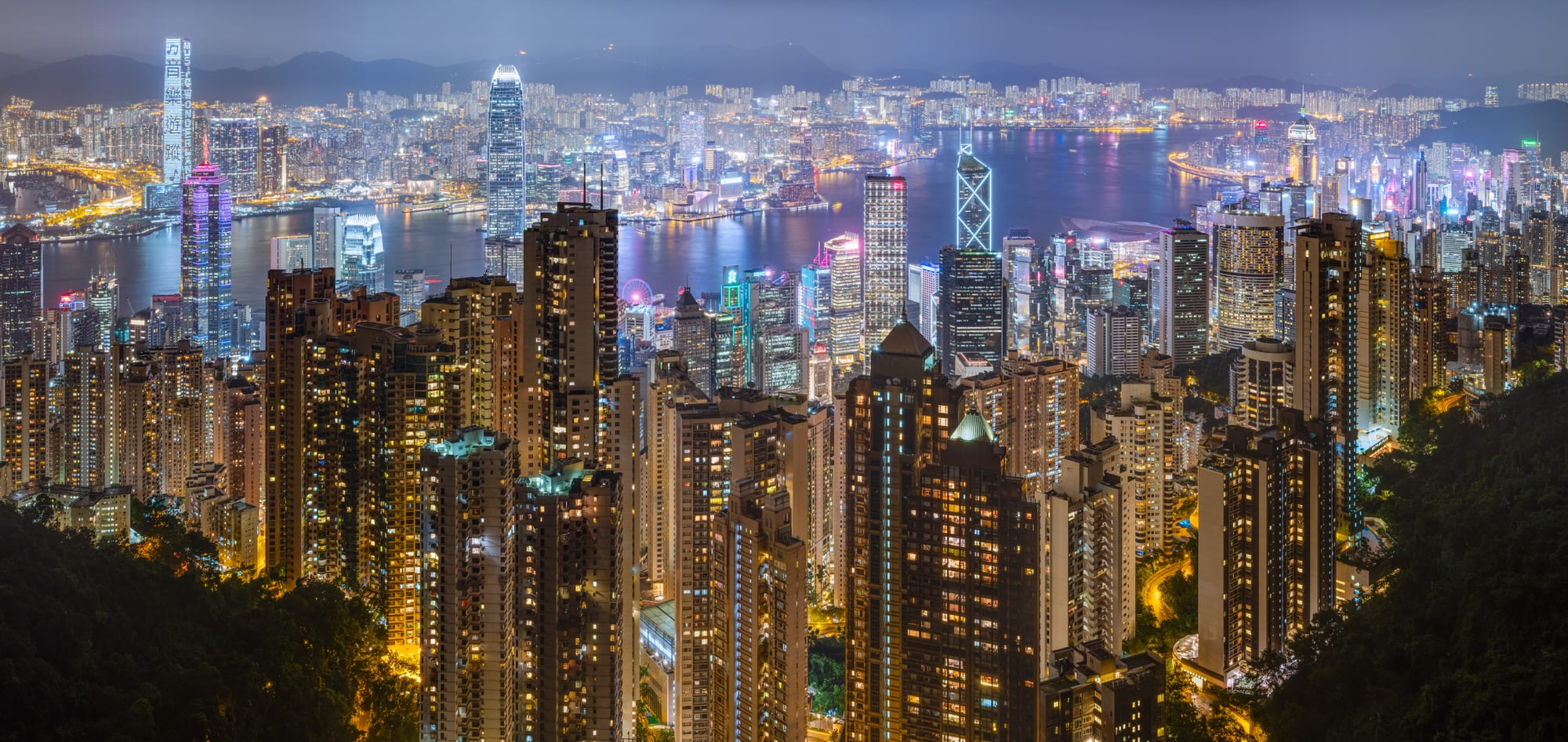 A dense wall of illuminated skyscrapers along a harbour at night, reflected in the water