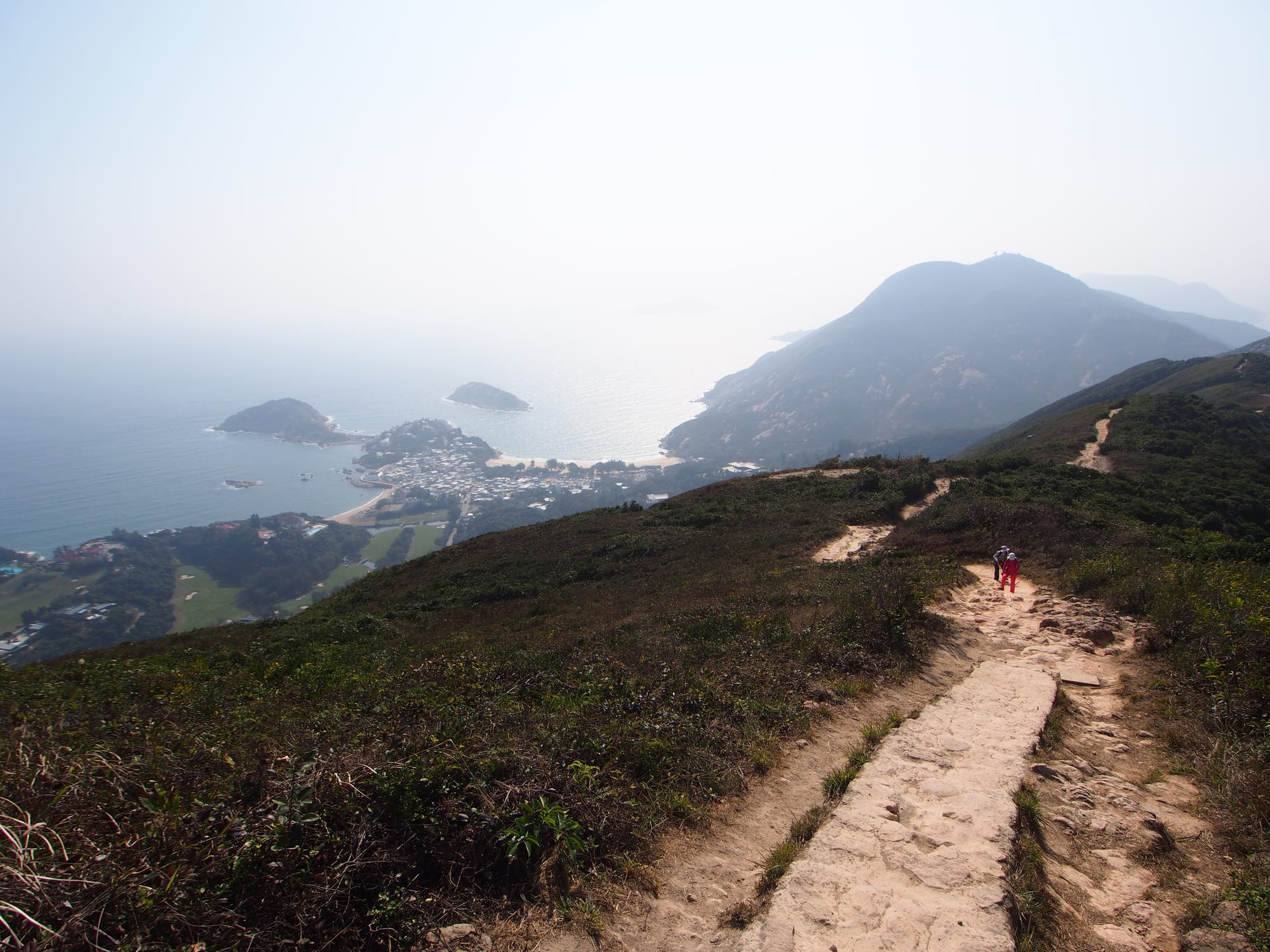 A ridge trail winding over grassy hills with the sea and islands beyond