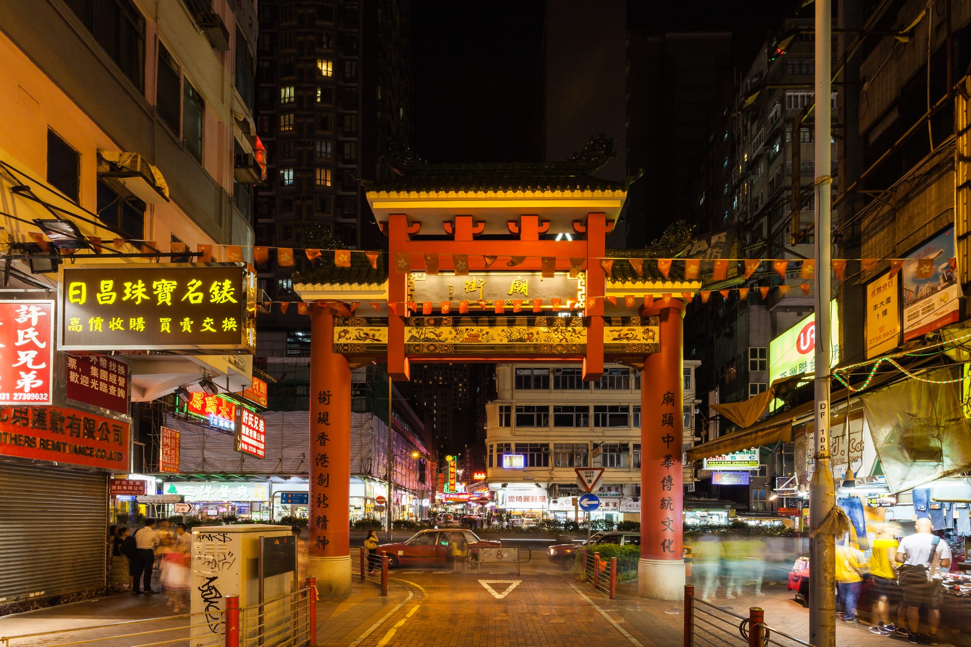 A night market street packed with red-lit stalls and crowds under neon signs
